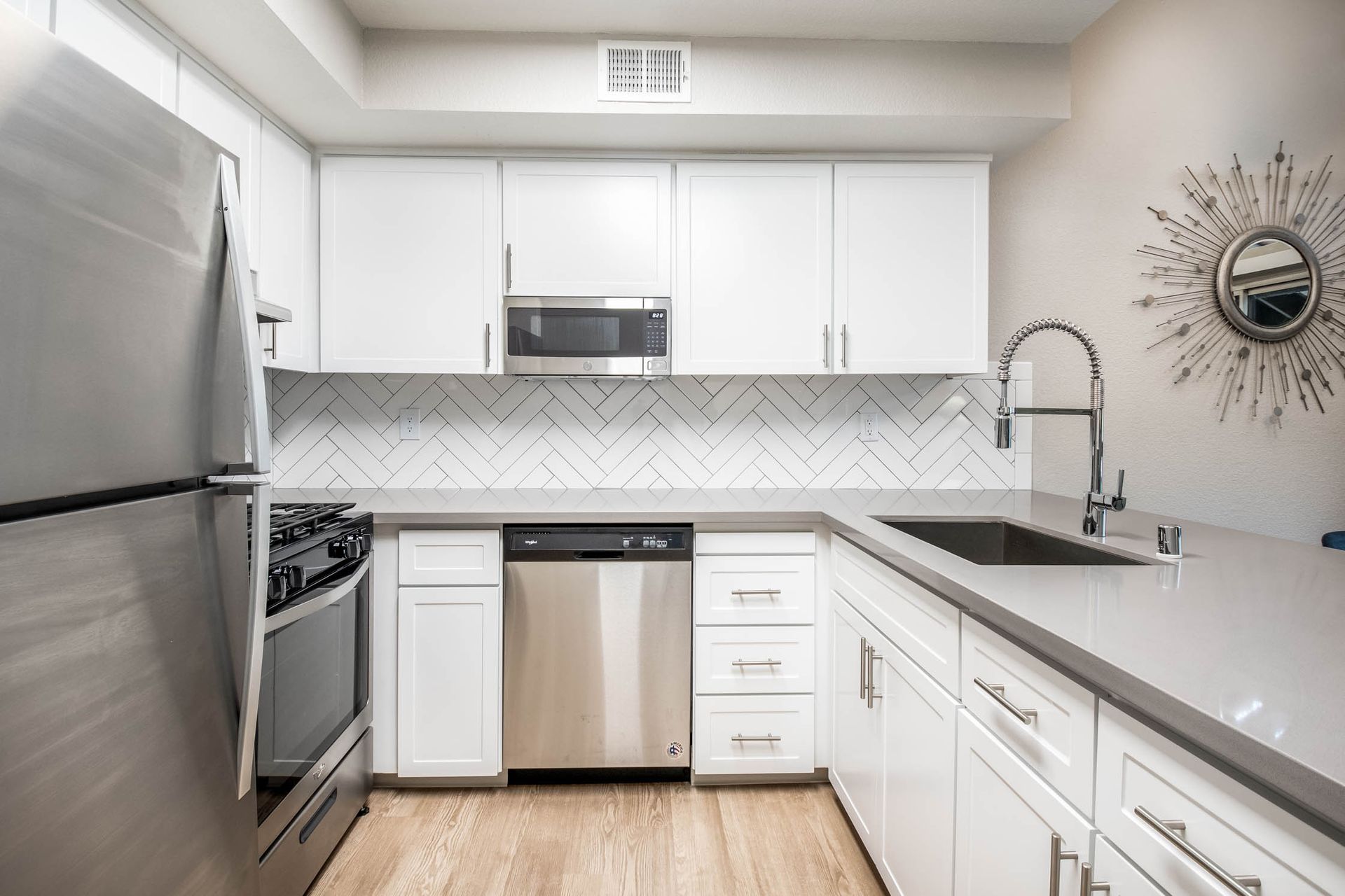 White modern kitchen with stainless steel appliances and a large sink.