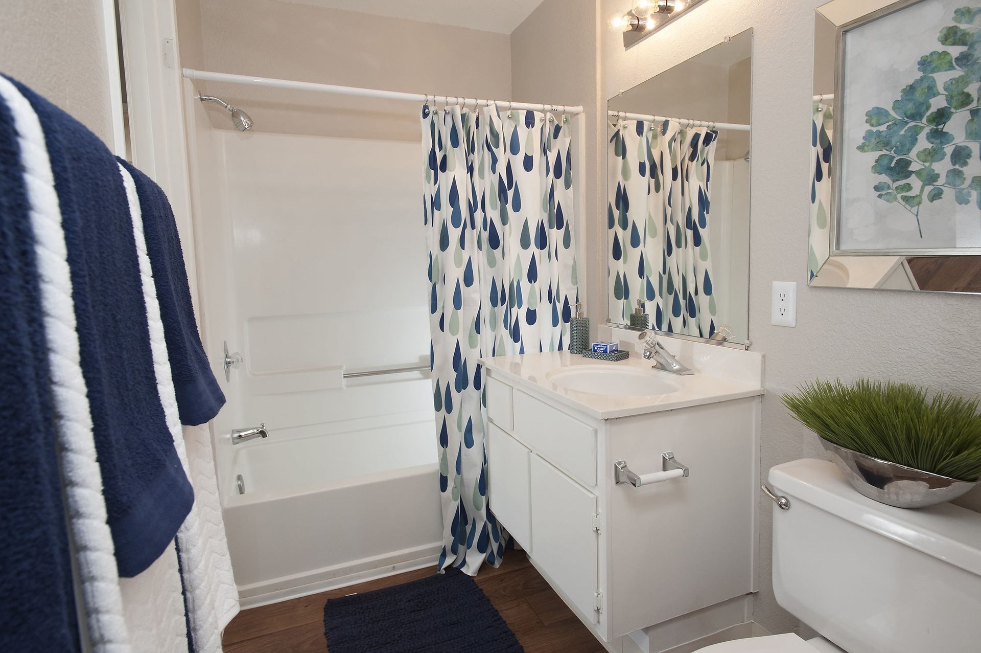 Bright bathroom with white vanity, mirror, tub/shower, and a blue teardrop-pattern shower curtain.