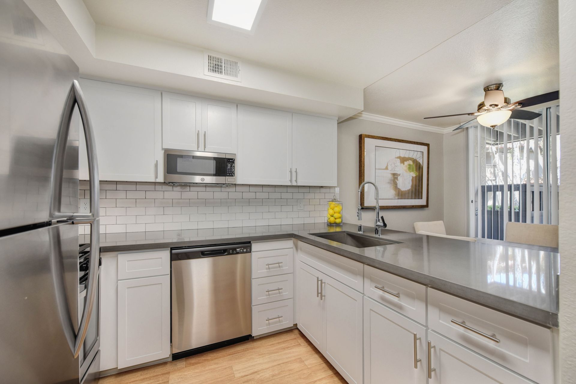Bright kitchen with white cabinets, stainless steel appliances, and an island with sink.