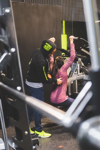 a man is helping a woman exercise on a machine in a gym .