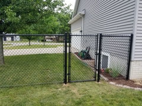 A chain link fence with a gate in front of a house.