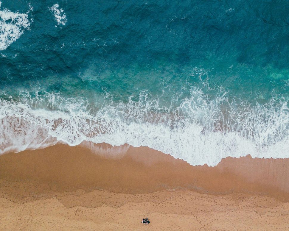 Aerial view of waves crashing against a sandy beach with a person walking along the shore.