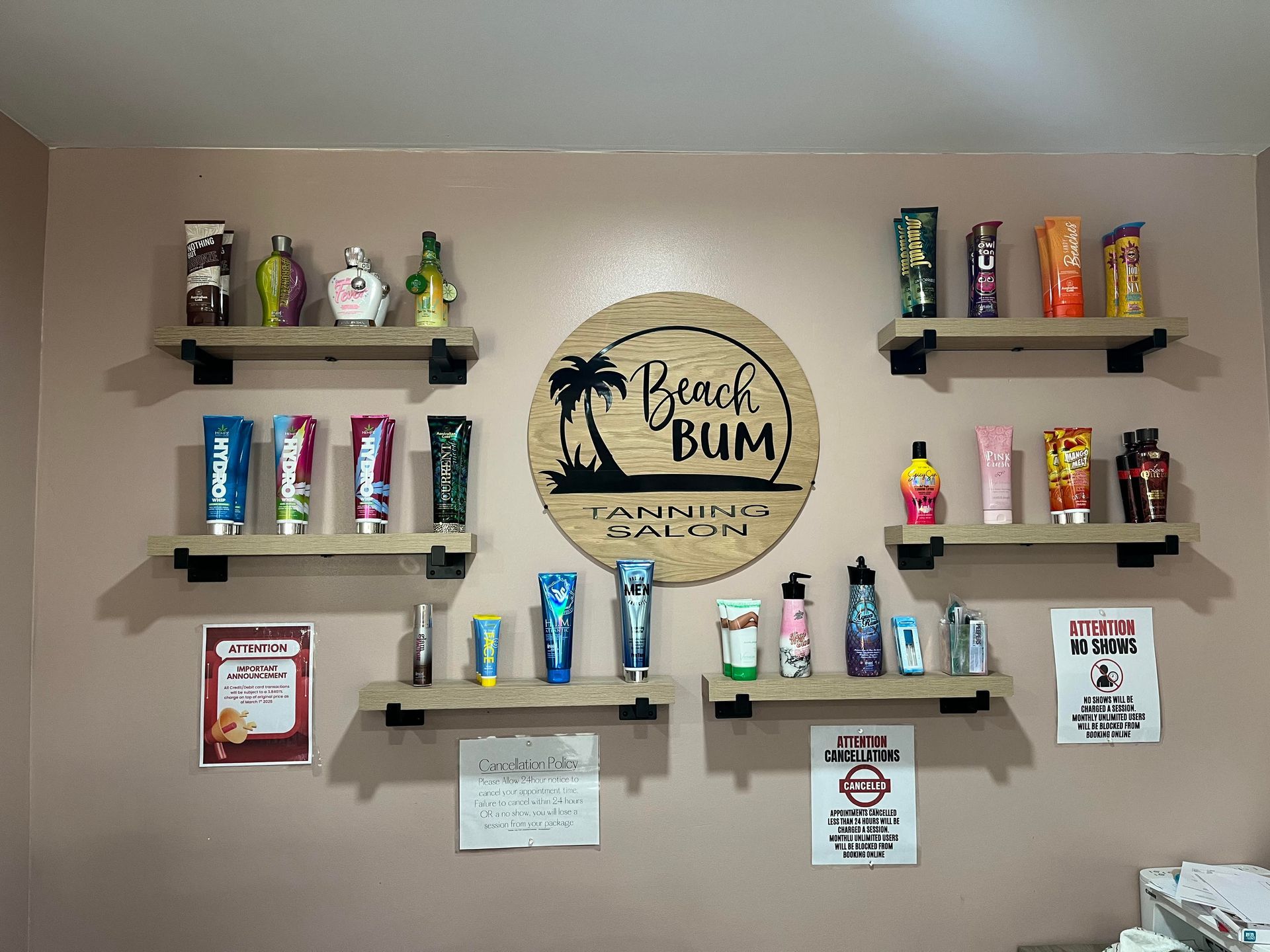 Wall display for Beach Bum tanning salon with assorted lotion bottles on wooden shelves surrounding a logo sign.