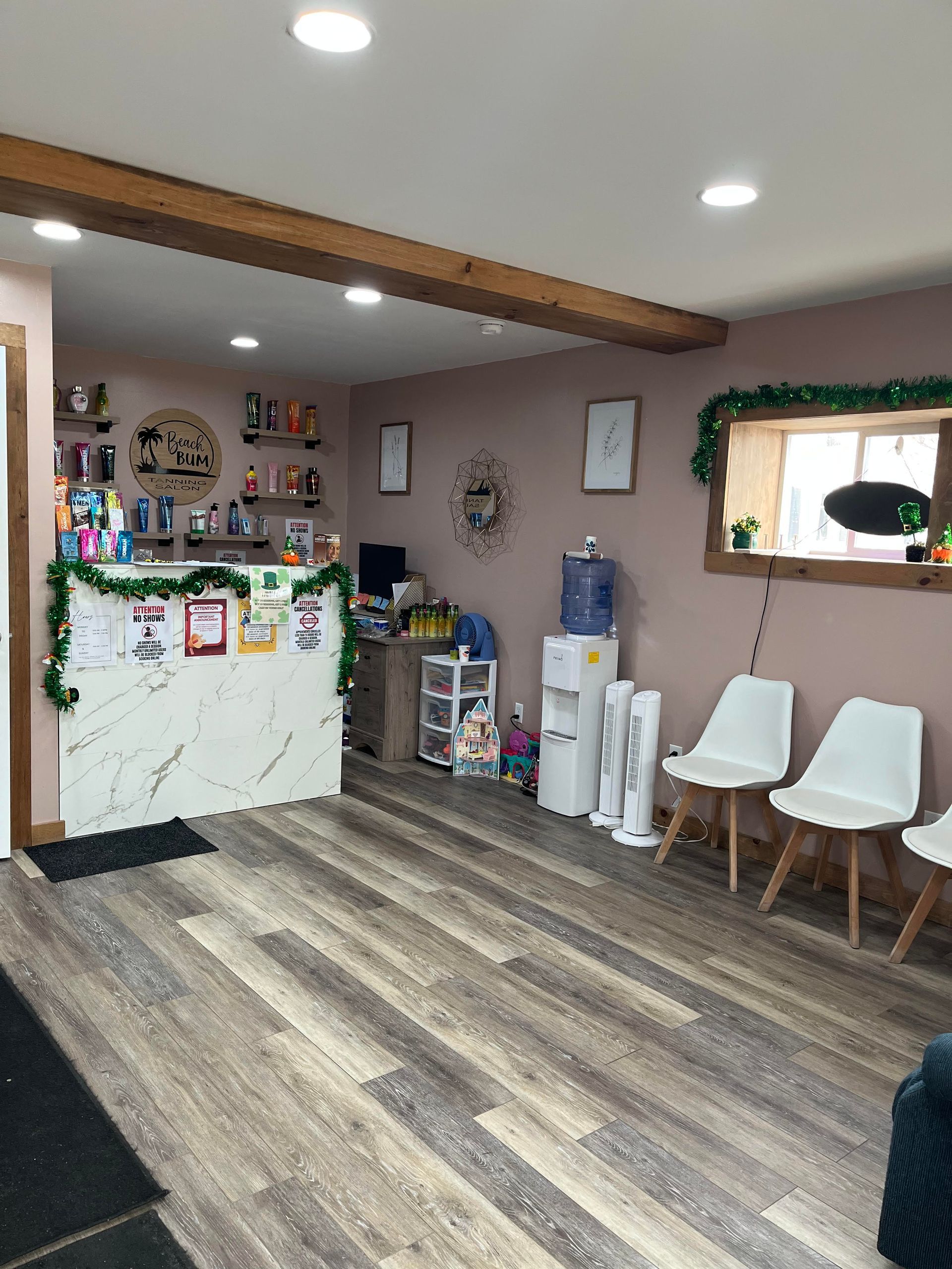 A reception area with a white marble desk, wood-look flooring, two white chairs, a water cooler, and decorative garland.