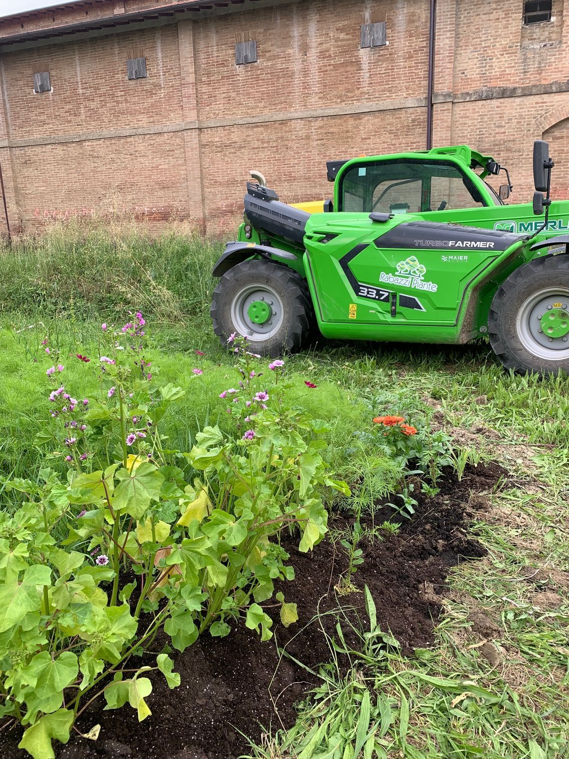 un trattore verde è parcheggiato in un campo erboso accanto a un edificio in mattoni.