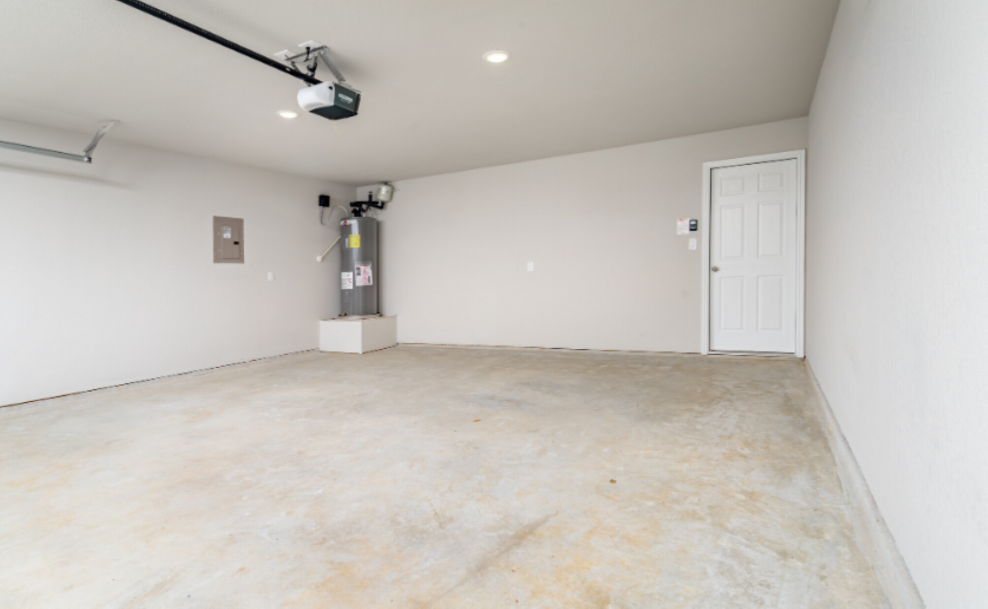 Empty garage with white walls, concrete floor, garage door opener, and water heater.