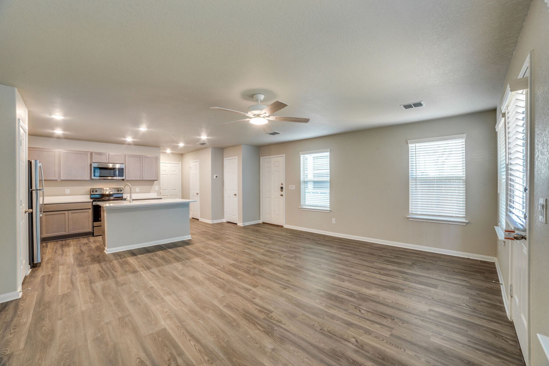 Open-concept living space with kitchen, island, and light gray walls, with wood-look flooring.