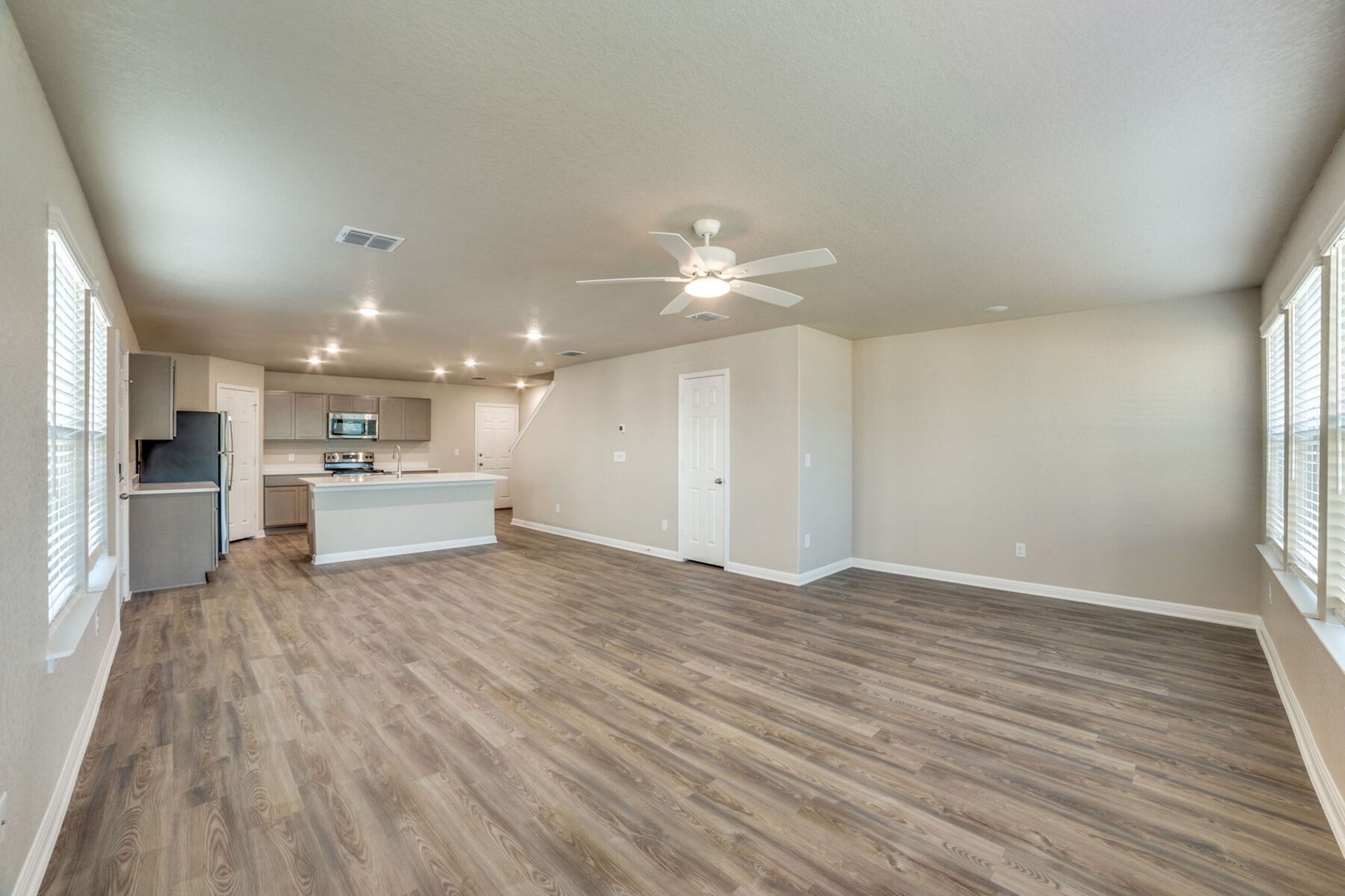 Open-plan living space with gray laminate floors, kitchen at the back, and large windows.