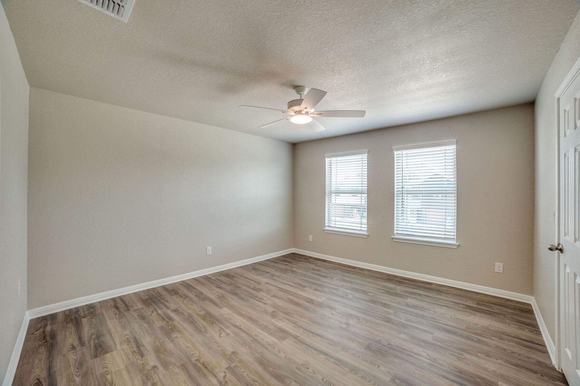 Empty room with wood-look flooring, two windows, ceiling fan, and neutral-colored walls.