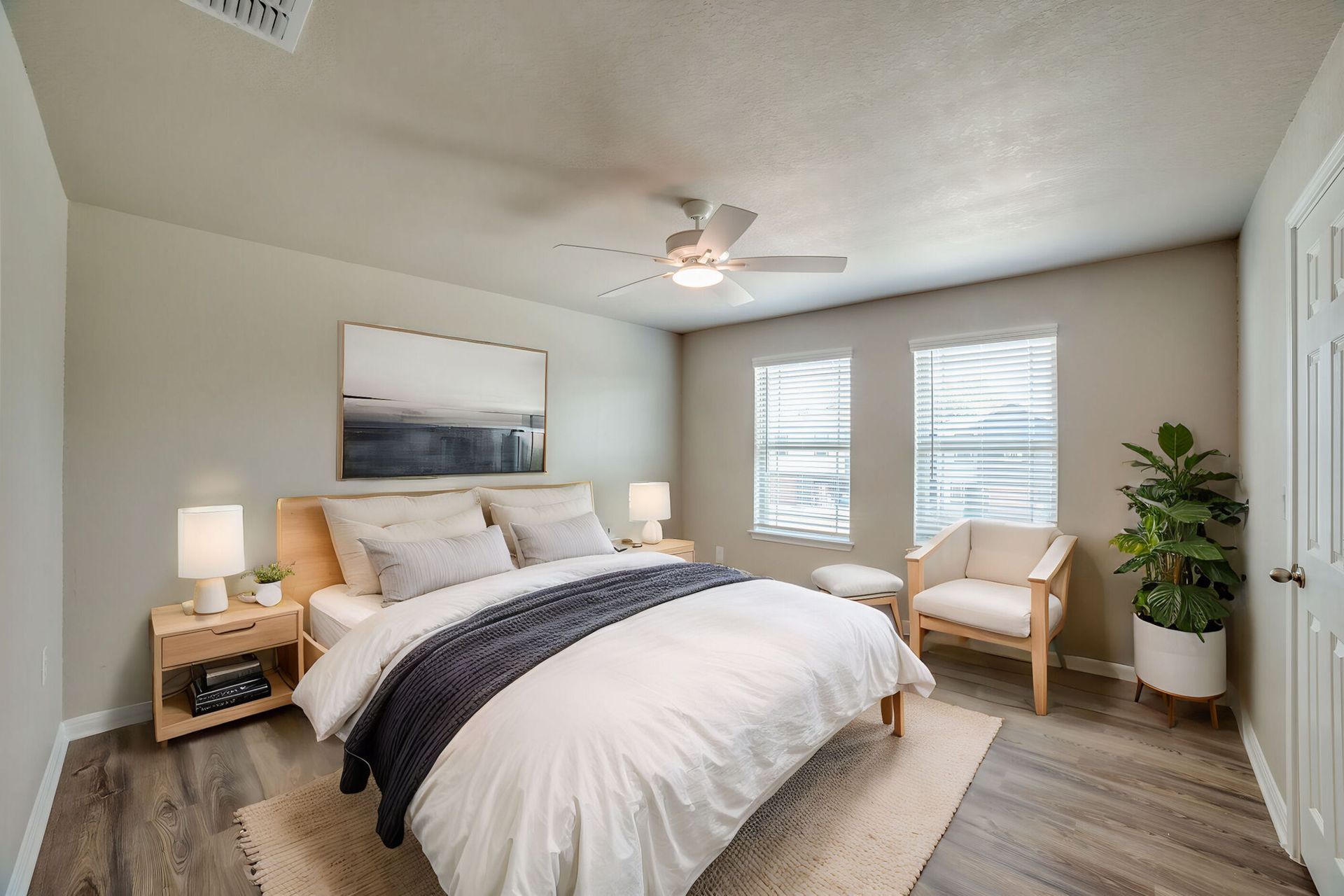Bedroom with a bed, armchair, artwork, and a potted plant. Neutral tones and natural light.
