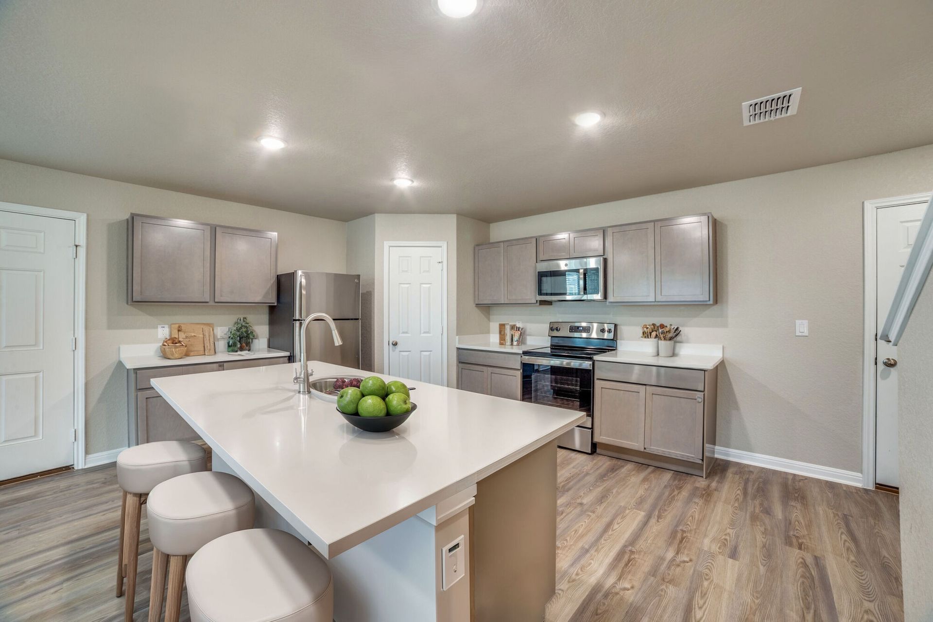 Kitchen with gray cabinets, white countertops, island with stools, and stainless steel appliances.