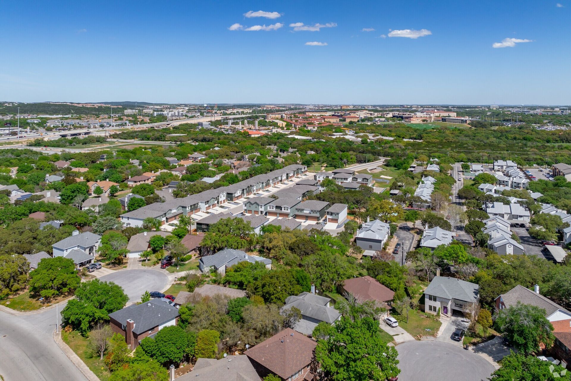 Aerial view of residential neighborhood with green trees and blue sky.