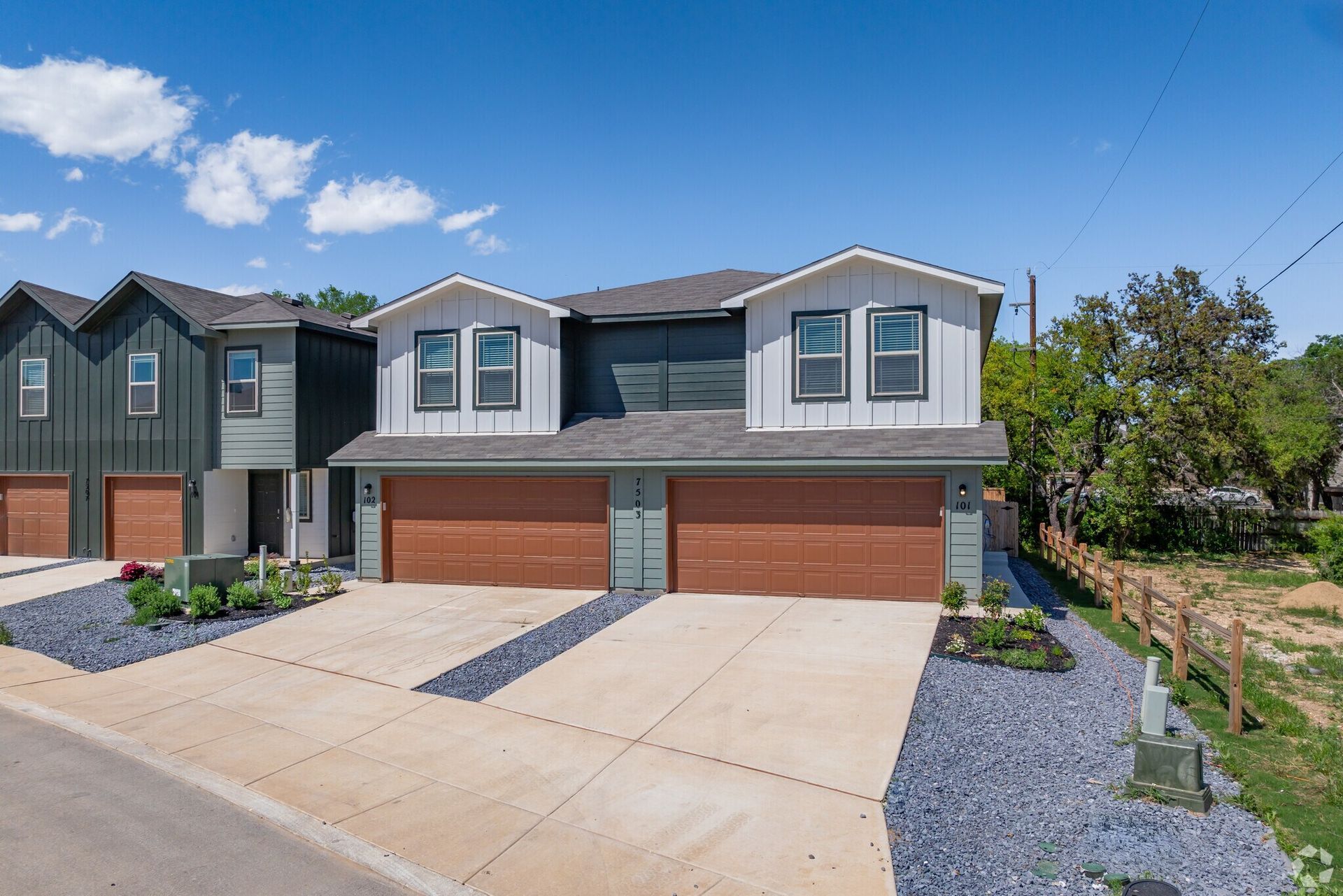 Modern two-story duplex with gray and brown exterior, blue gravel landscaping, and blue sky.