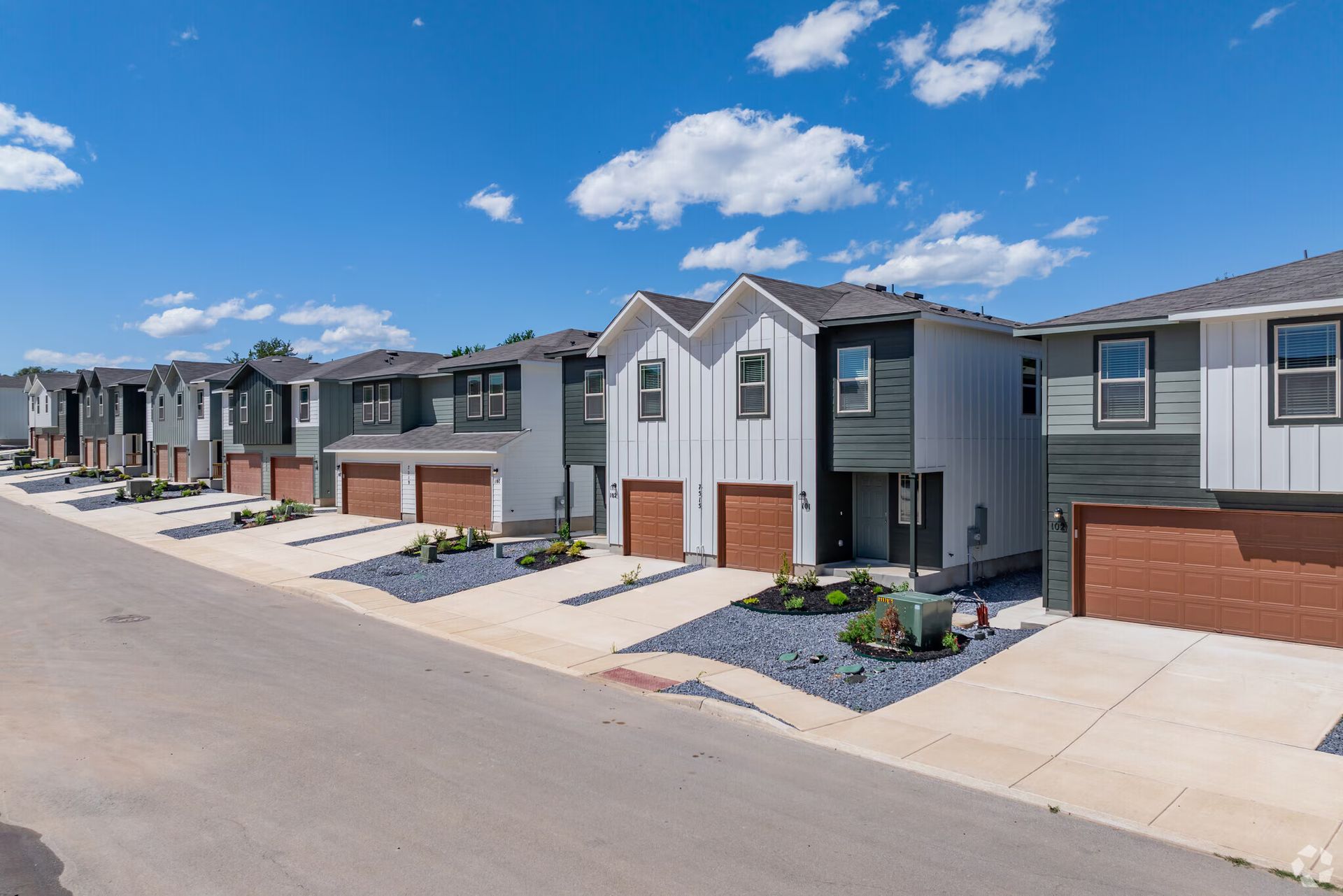 Row of modern townhomes with gray and green siding, brown garage doors, and blue gravel landscaping.