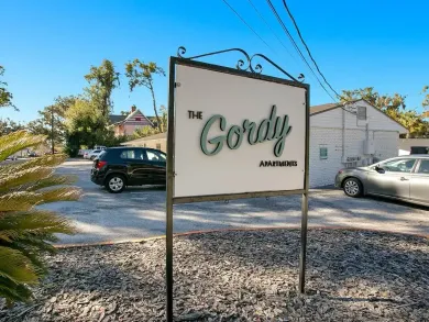 A sign for the gordy apartment building is hanging from a metal pole.