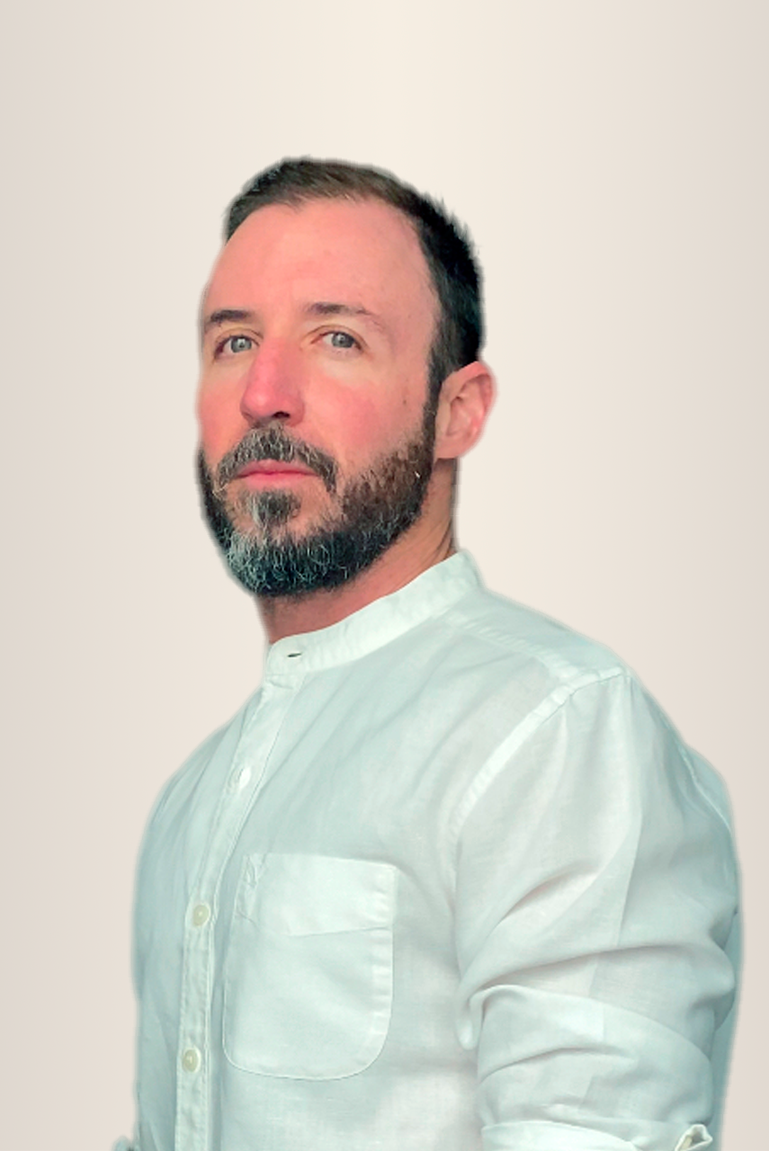 Hombre con cabello y barba de color castaño claro, vestido con una camisa blanca abotonada, sobre un fondo pálido.