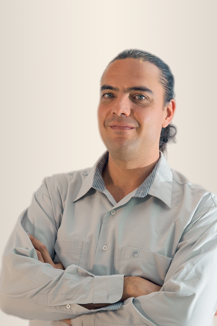 Un hombre con cabello corto y barba de color castaño sonríe, vistiendo una camisa azul con cuello y bolsillo estampados.