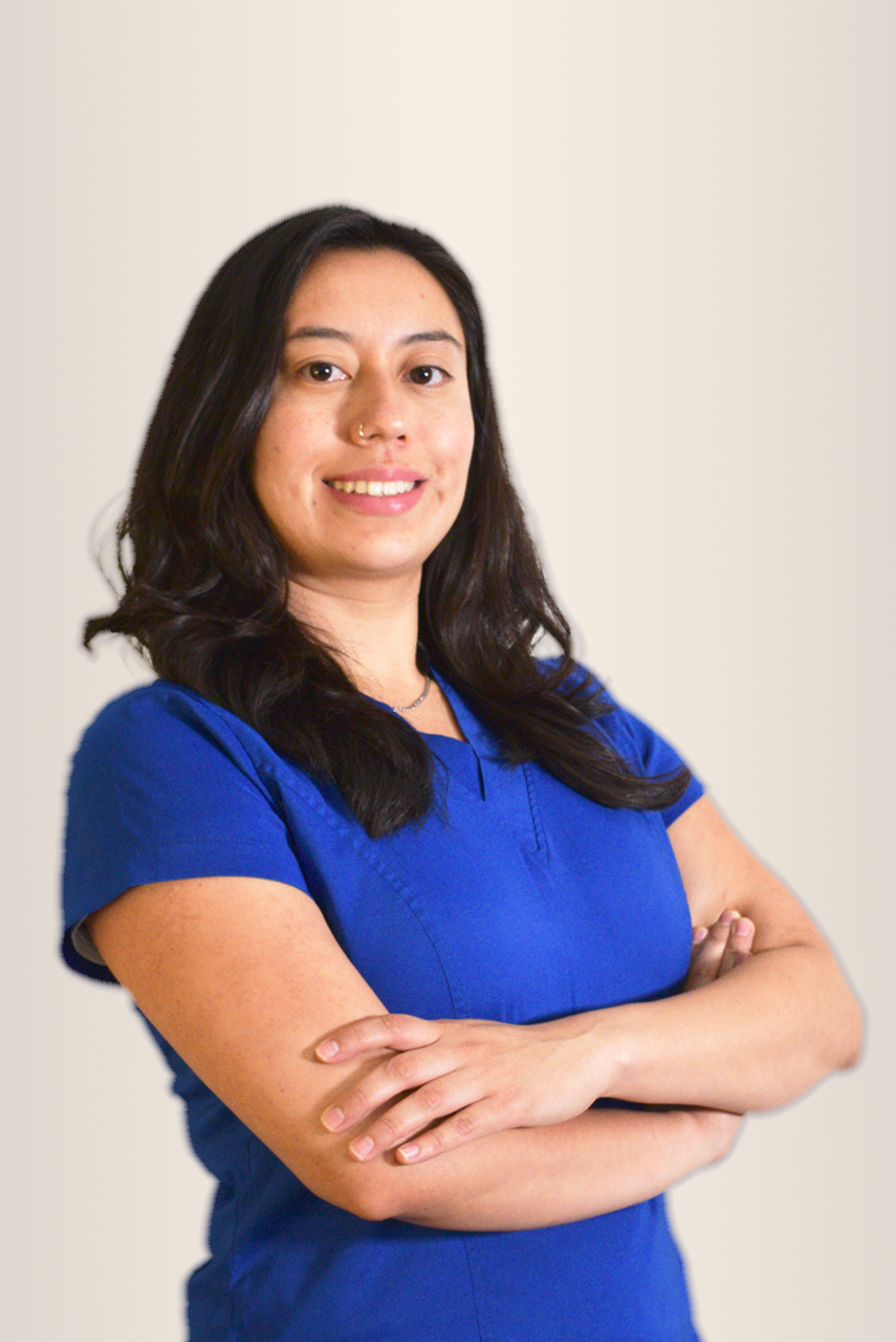 Mujer con bata blanca sonriendo, mirando a la cámara. Fondo neutro.