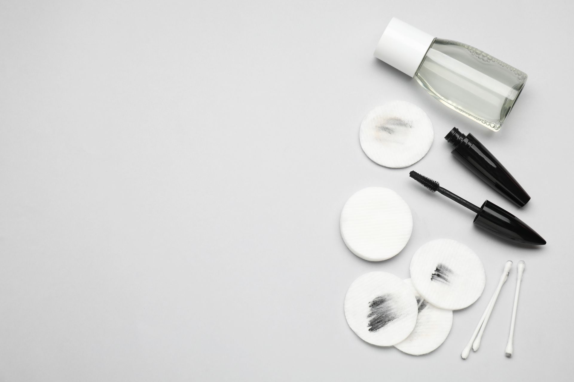 A bottle of makeup remover , mascara , cotton swabs and cotton pads on a white background.