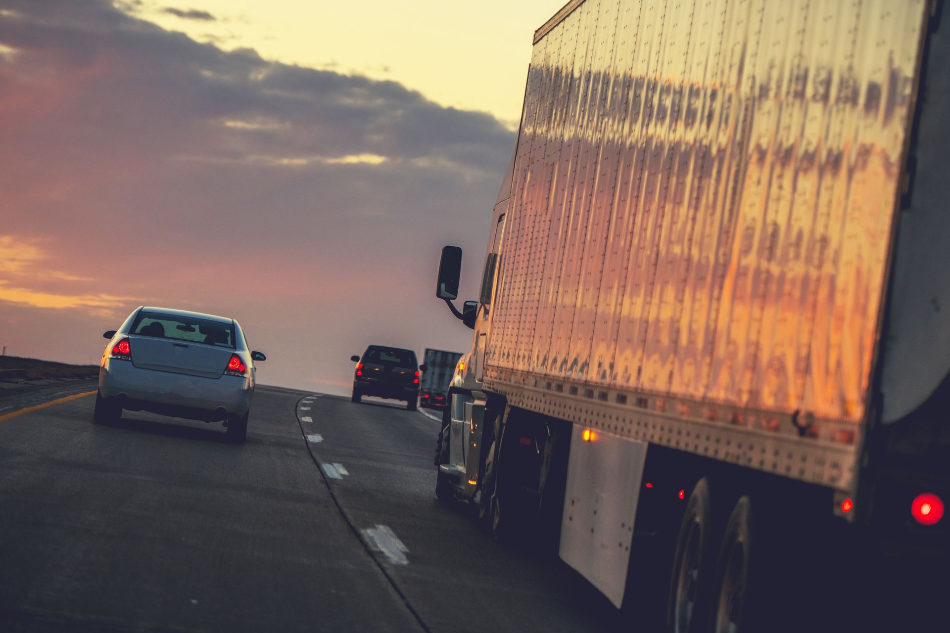 A truck and cars are driving down a highway at sunset.