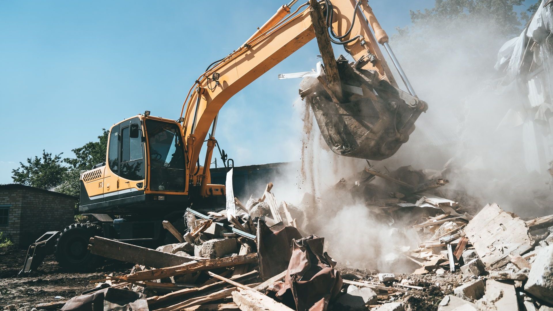 Une excavatrice jaune démolit un bâtiment.