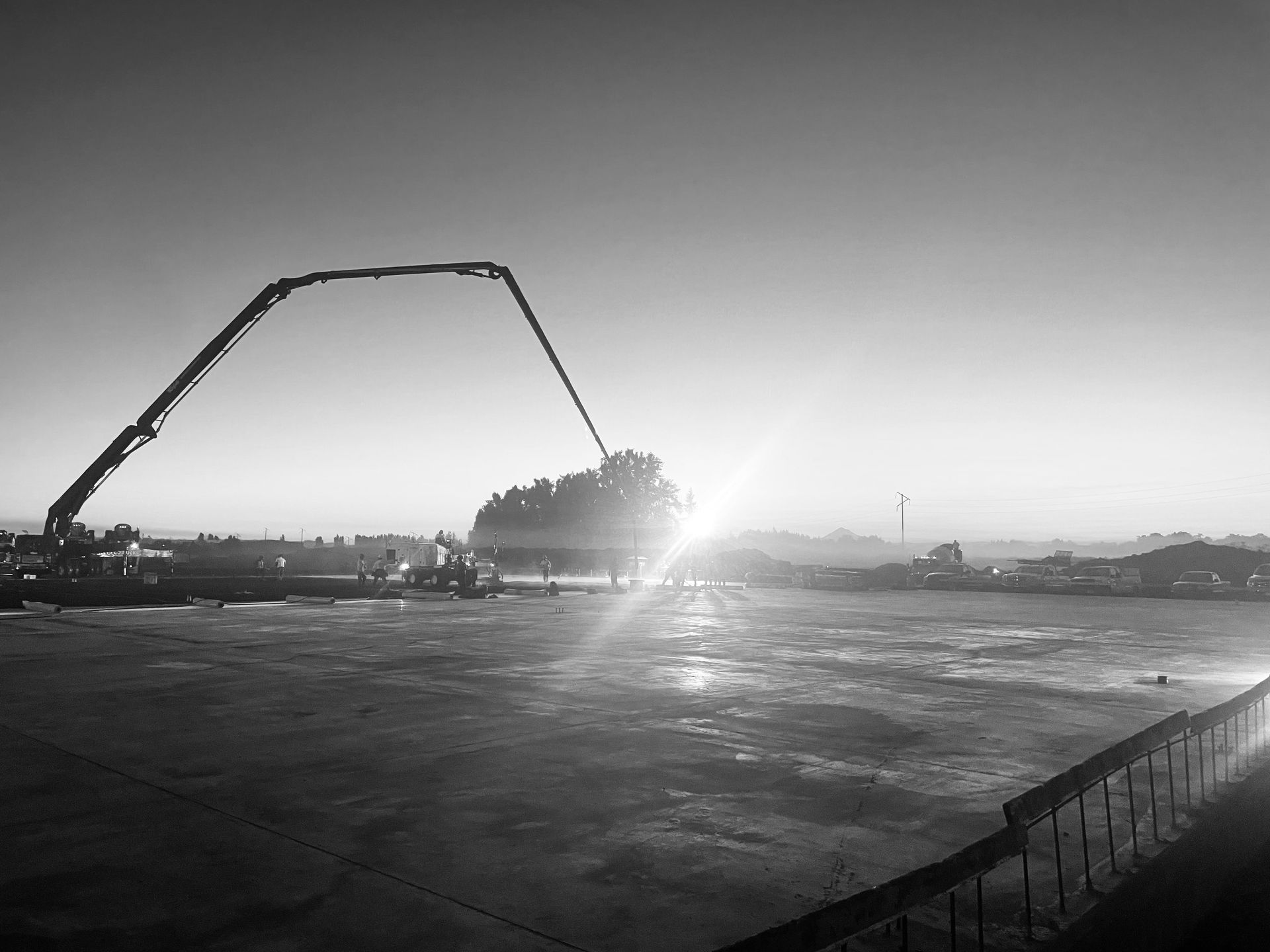 Construction site with a concrete pump arm pouring concrete into a formwork, setting sun in the background.