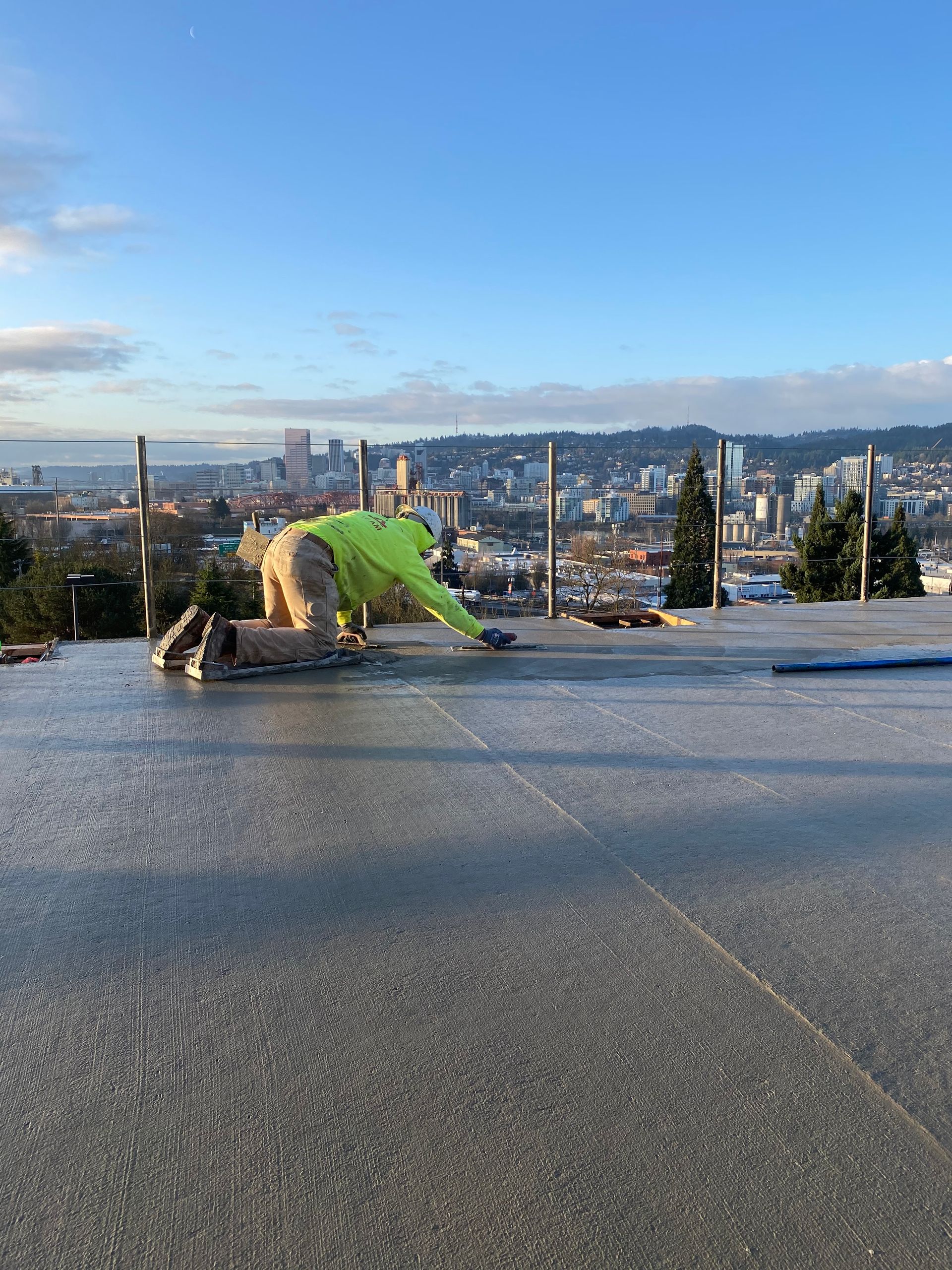 Person in neon green working on a concrete surface with city in the background. Bright sky.