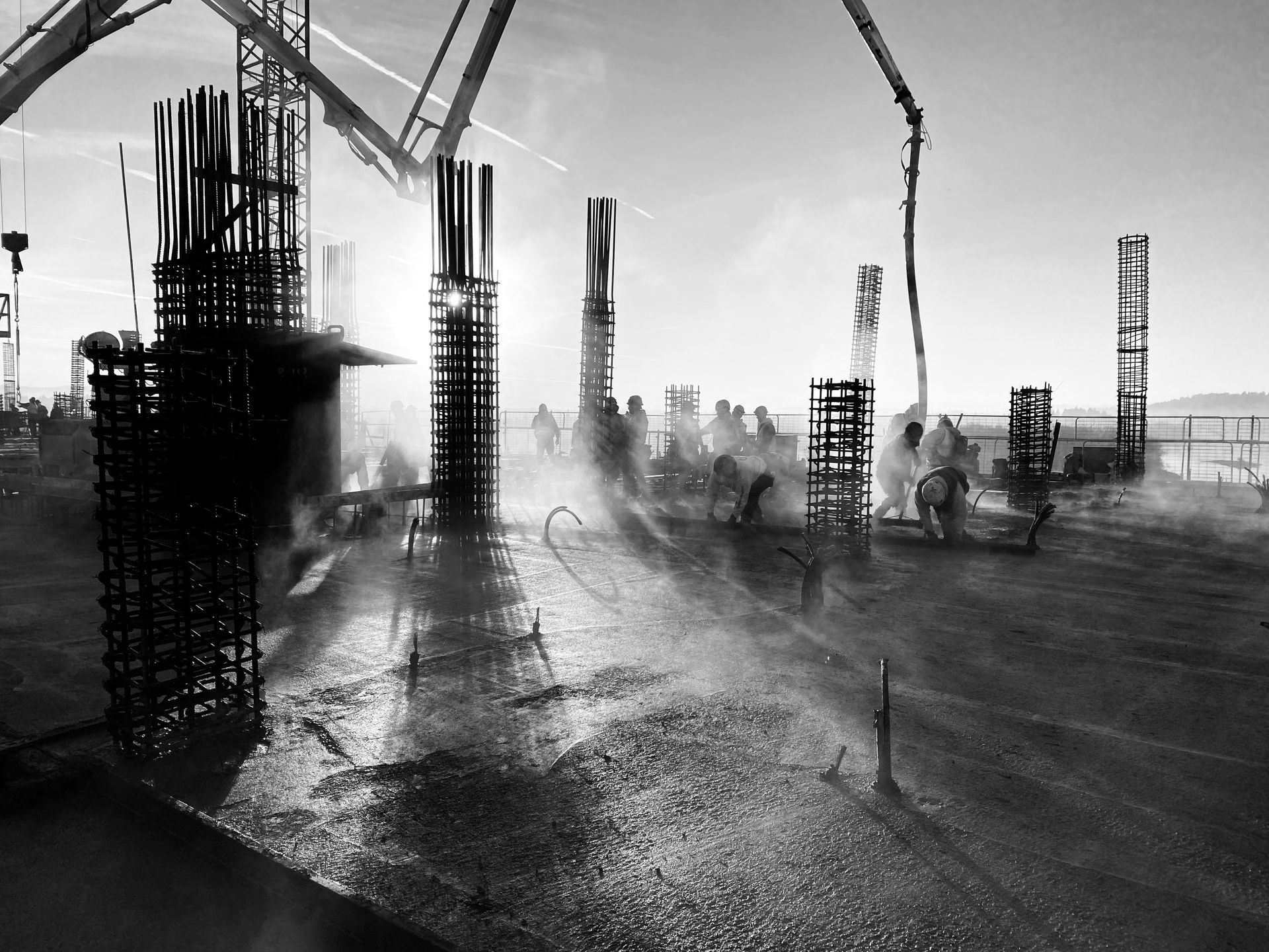 Construction site with workers, concrete pillars, and cement being poured; sun shining.