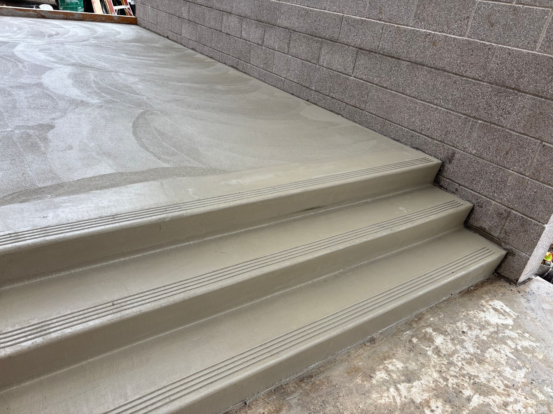 Concrete steps with textured edges lead to a concrete landing, near a textured wall.