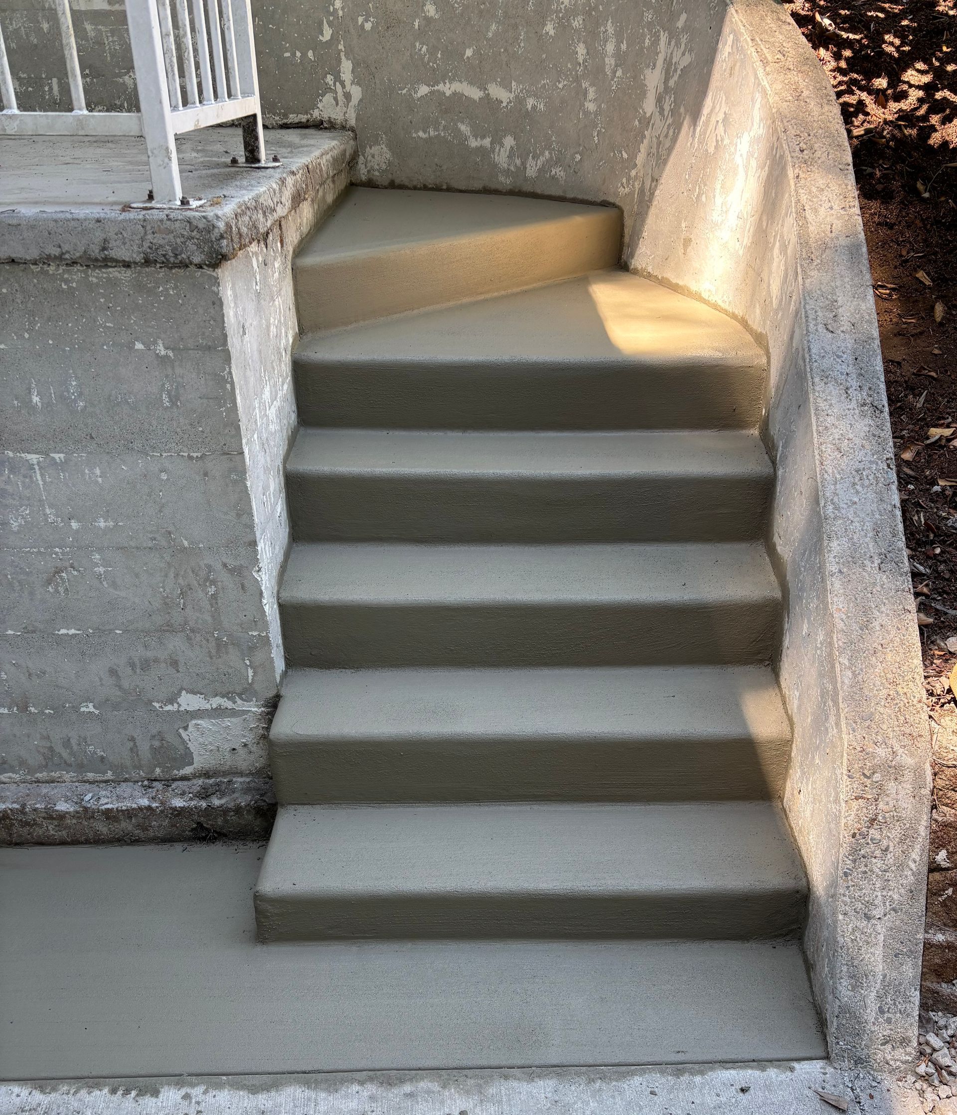 Concrete steps leading up to a landing with a white railing. Gray steps and walls.