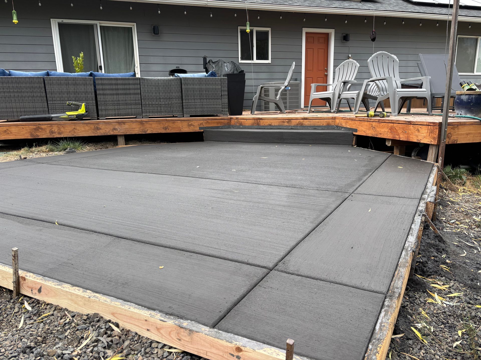 Freshly poured concrete patio with wooden framing, next to a house with a deck.