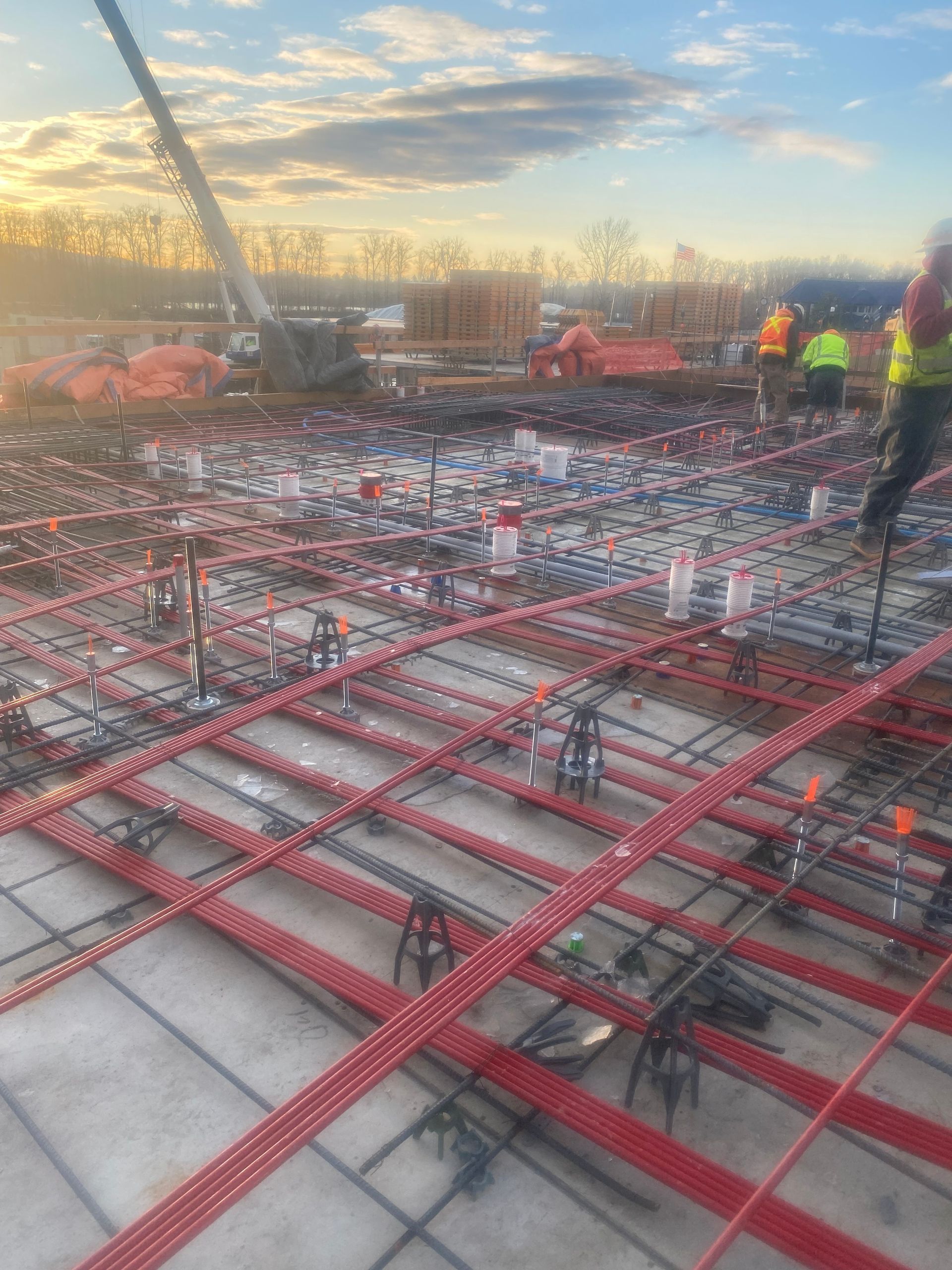 Construction site with red rebar grid, workers in high-vis vests, and crane.