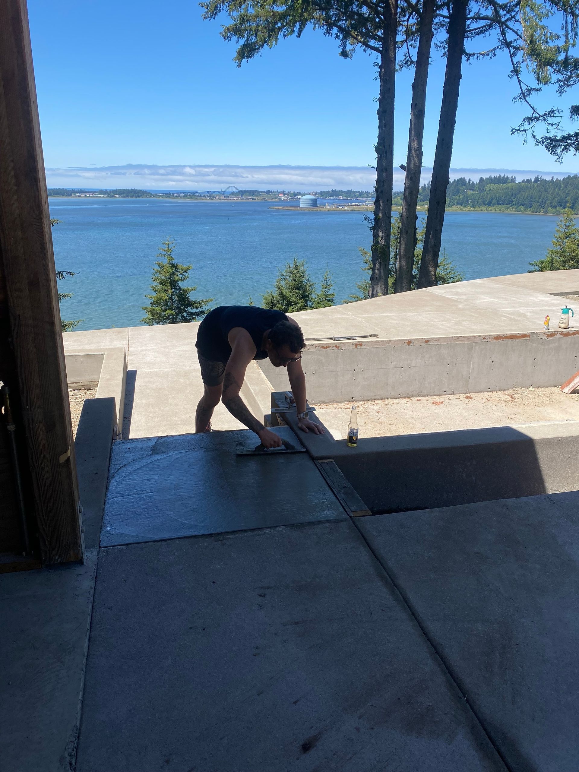Person smoothing concrete on a patio overlooking a body of water on a sunny day.
