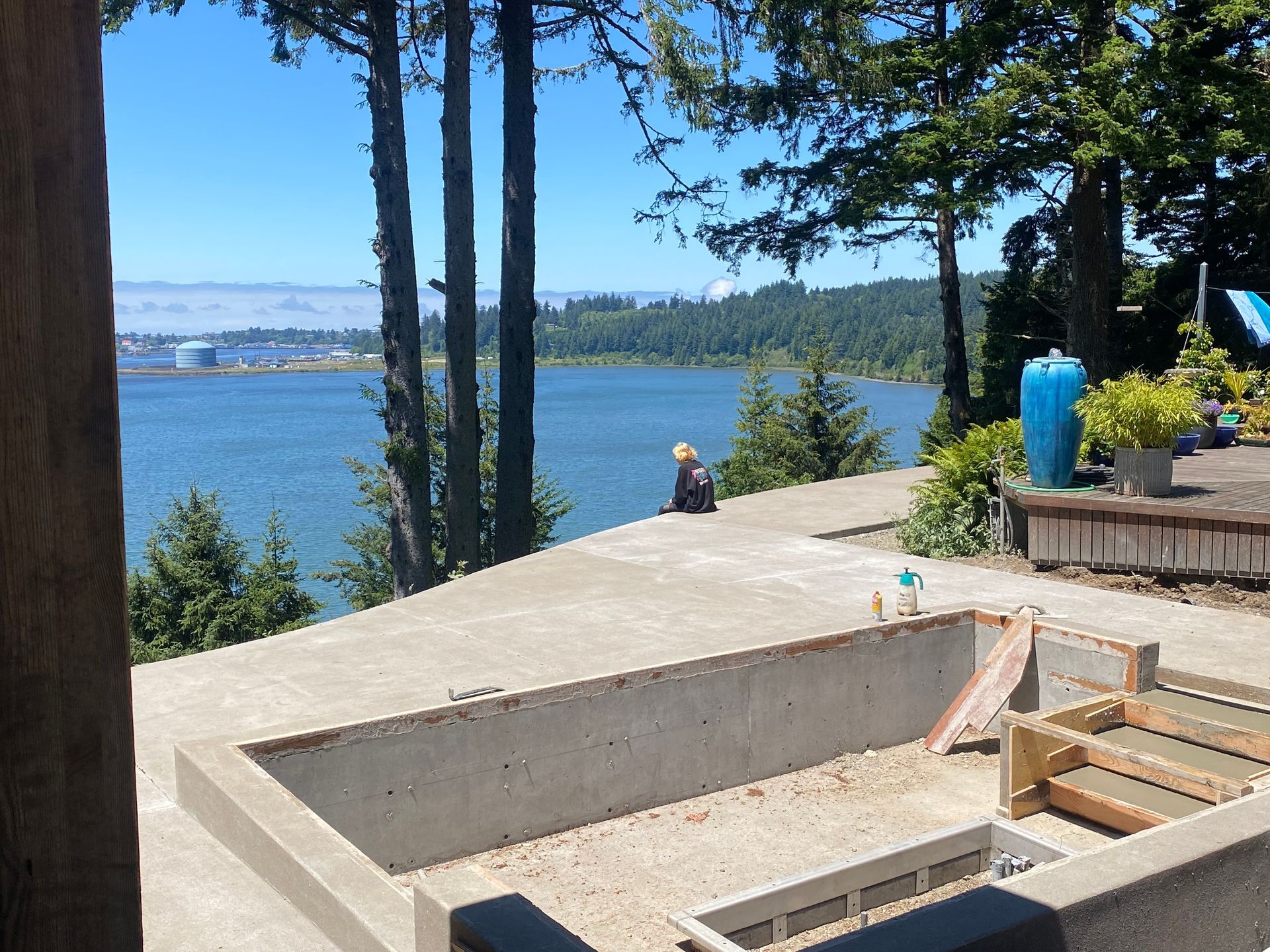 Concrete patio overlooking a lake; person sitting, trees, blue sky.
