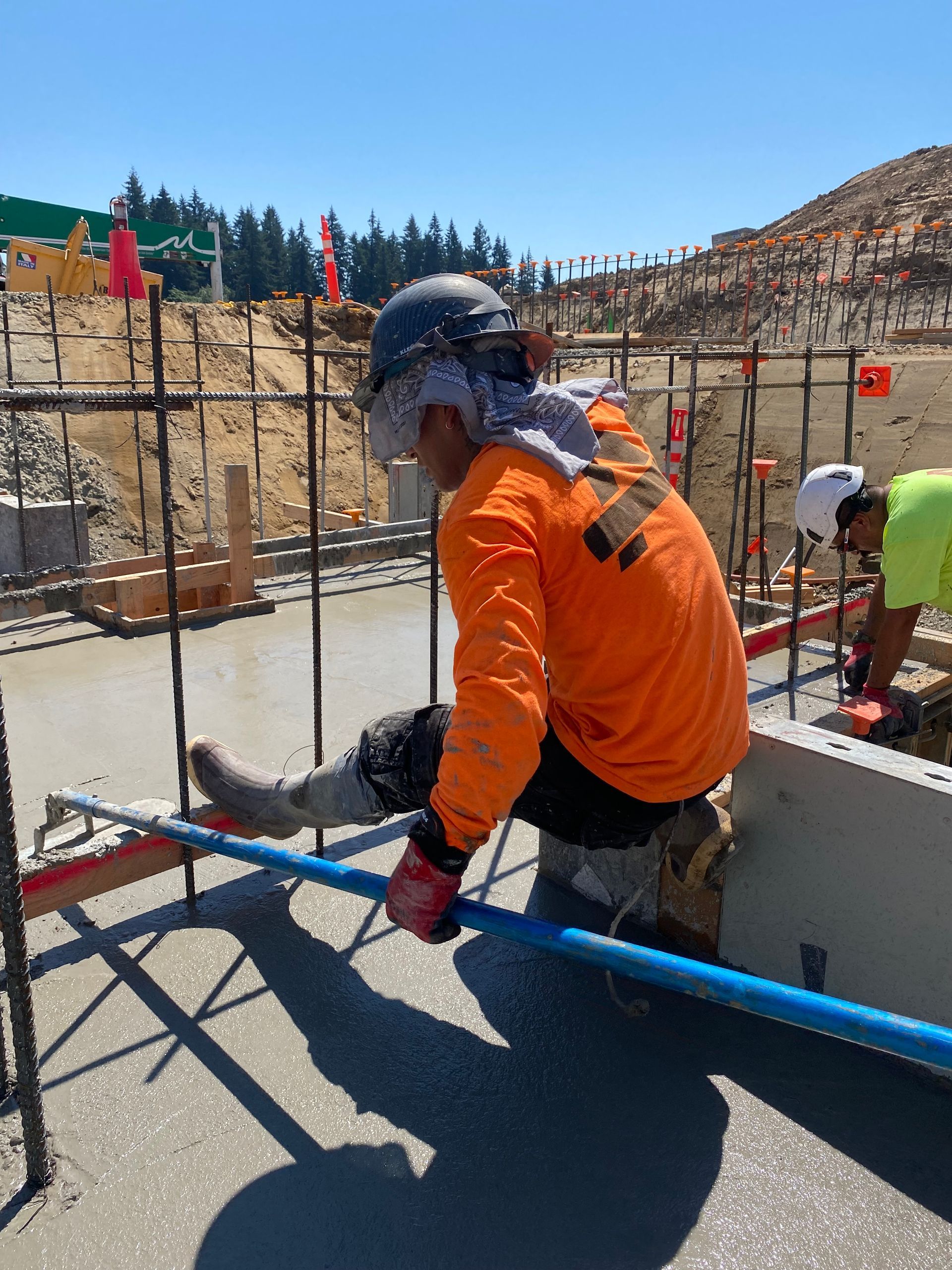 Construction worker smoothing wet concrete with a long tool on a sunny day.