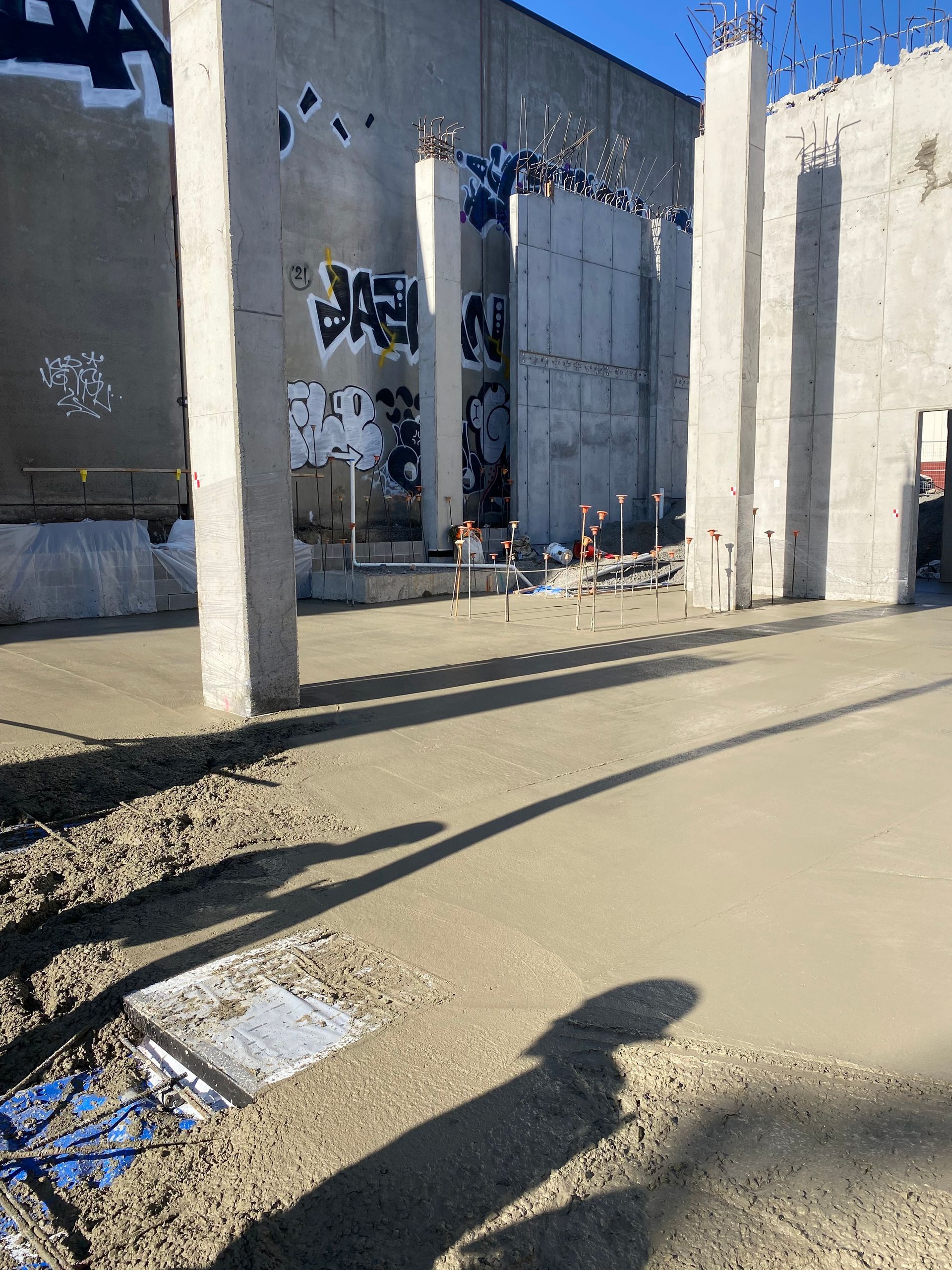 Construction site: concrete floor, concrete pillars, wall with graffiti, sunlight and shadows.