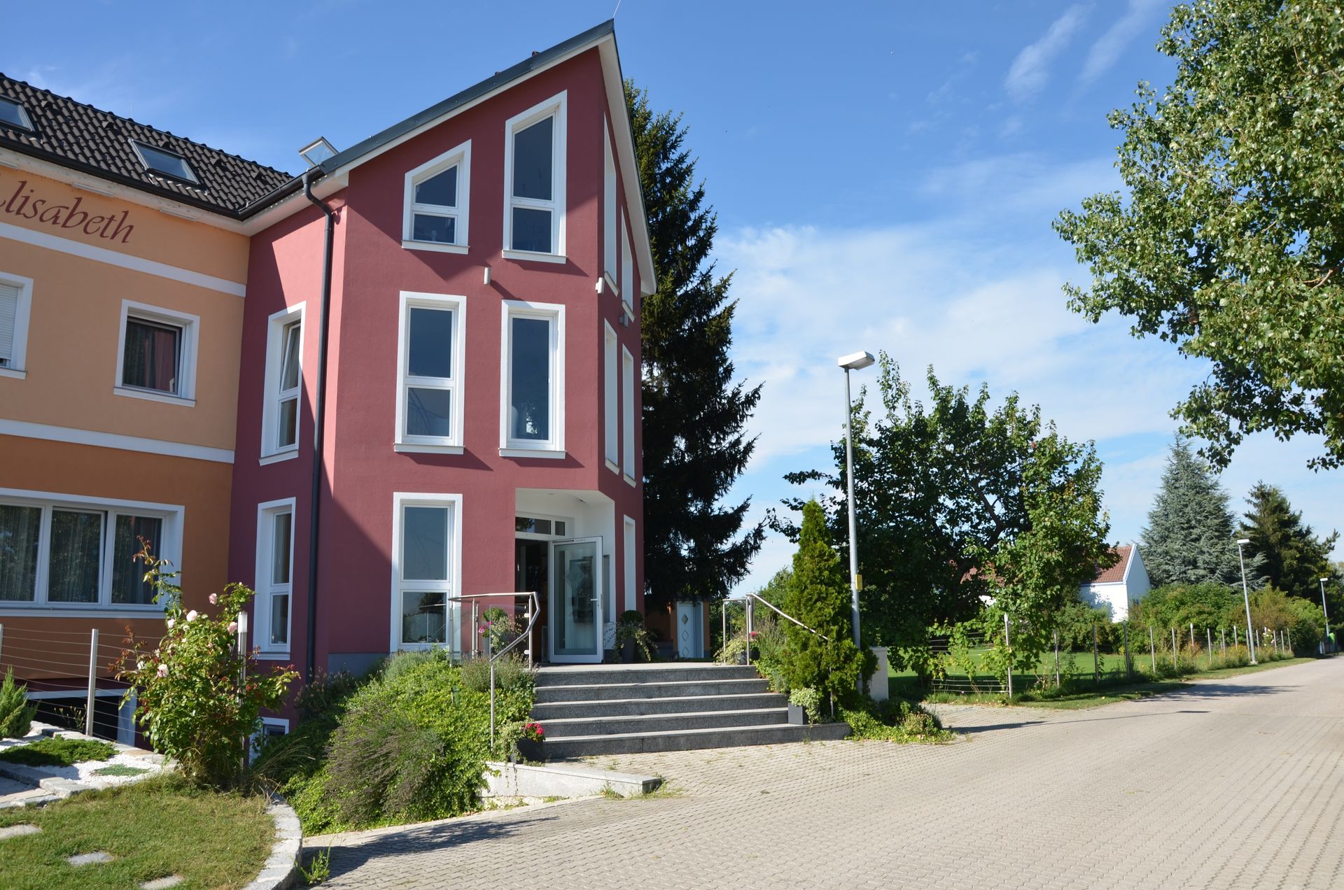 Hotel Maria von Außen, Stiegen führen zum Eingang. Das Haus hat eine hellrote Fassade. 