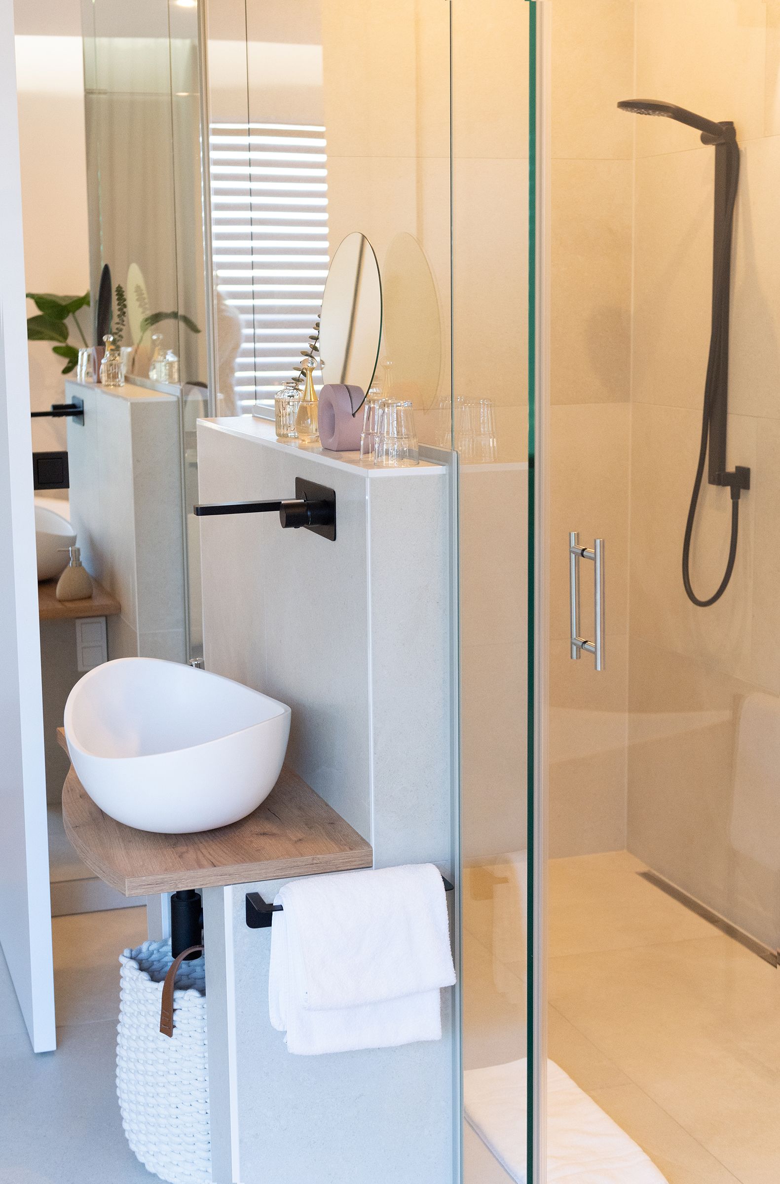 Offener Badezimmerbereich, freistehender Badewanne und begehbare Glasdusche. Die Armaturen und Regendusche sind schwarz. An Wand und Decke der Dusche ist eine indirekte Beleuchtung.