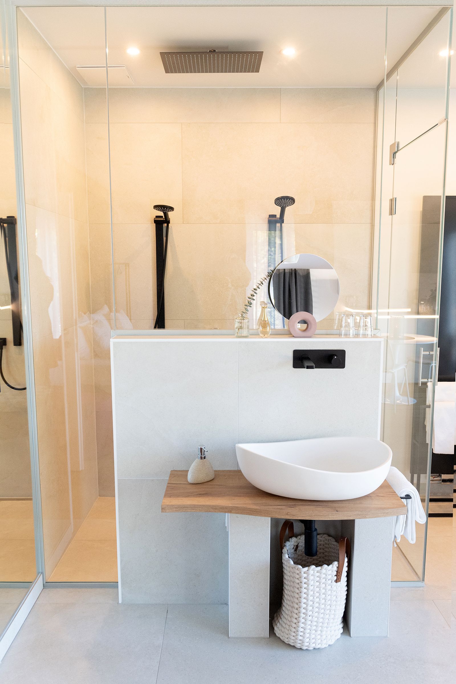 Offener Badezimmerbereich und begehbare Glasdusche. Die Armaturen und Regendusche sind schwarz. An Wand und Decke der Dusche ist eine indirekte Beleuchtung.