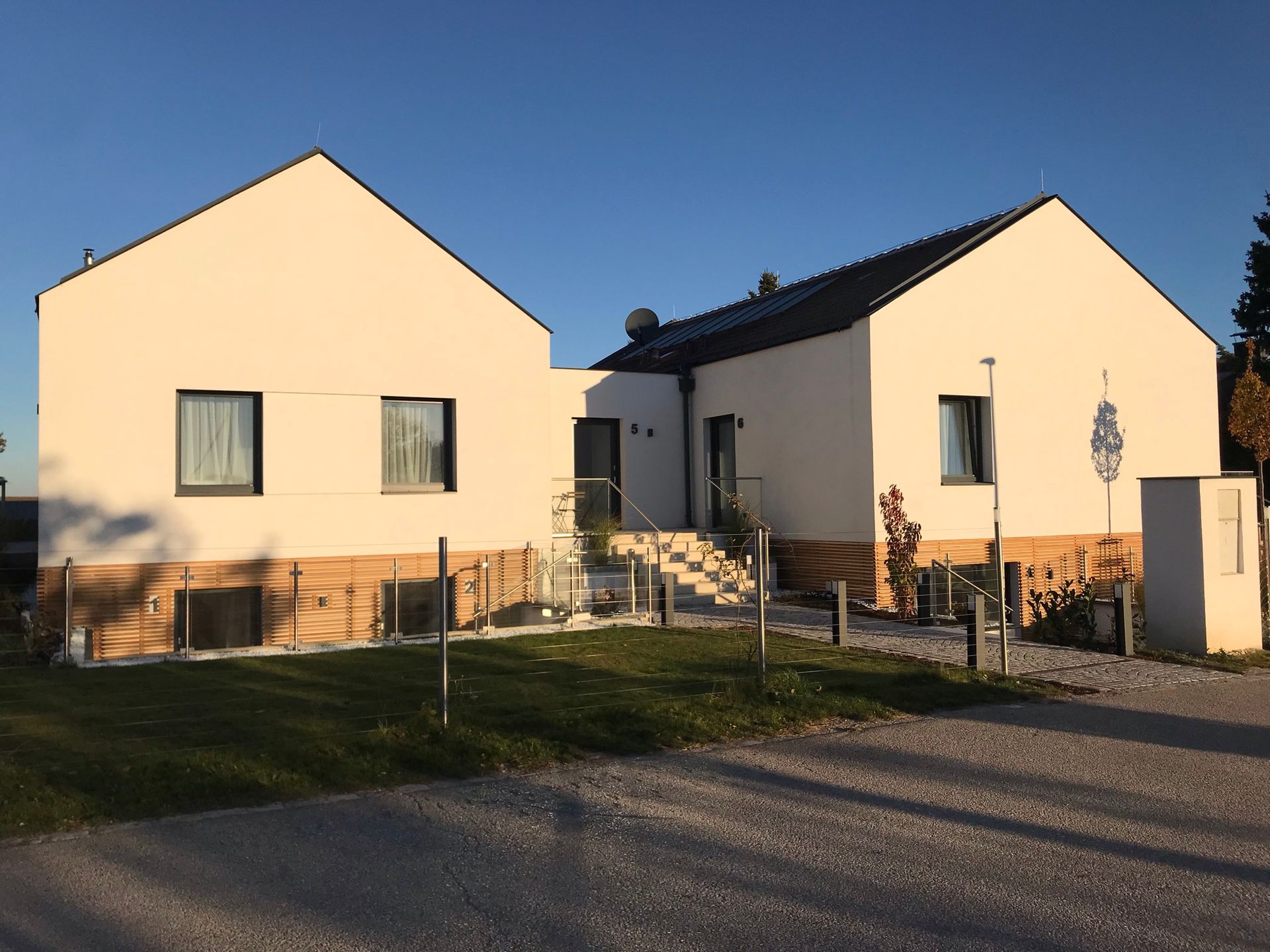 Außenansicht frontal bei Sonnenaufgang. Großes weißes haus mit Holzelementen. ein Pflasterstein Weg führt zu Appartment 1, 2, 3, 6.
Der angrenzende Rasen ist gepflegt.