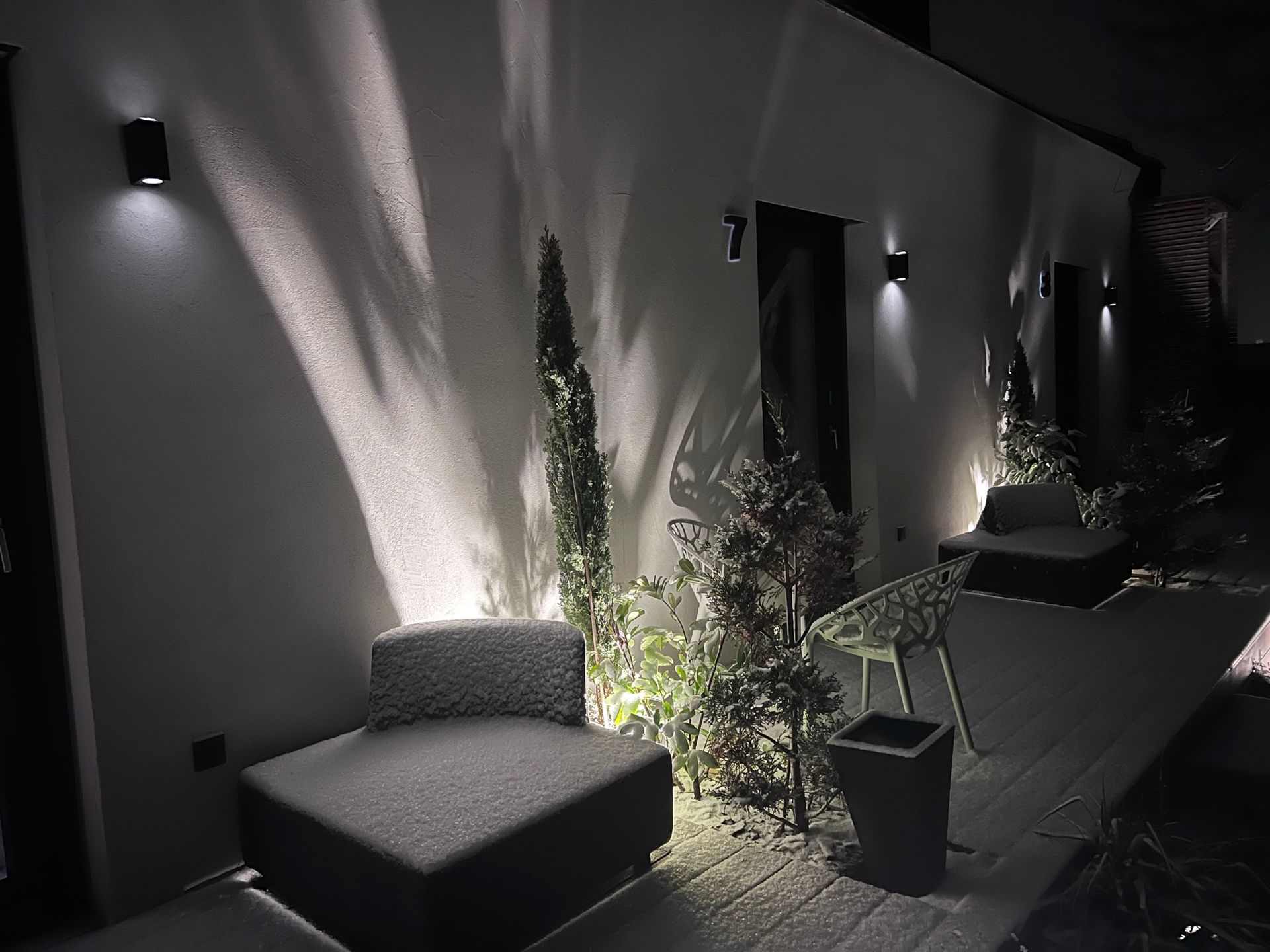 Außenansicht bei Nacht der Holzterrassen von Apartment 7 und 8 im Winter. Jede Terrasse hat einen grauen Stoffsessel und Pflanzen, welche mit Schnee bedeckt sind. Hinter den Sesseln ist eine indirekte Beleuchtung. 