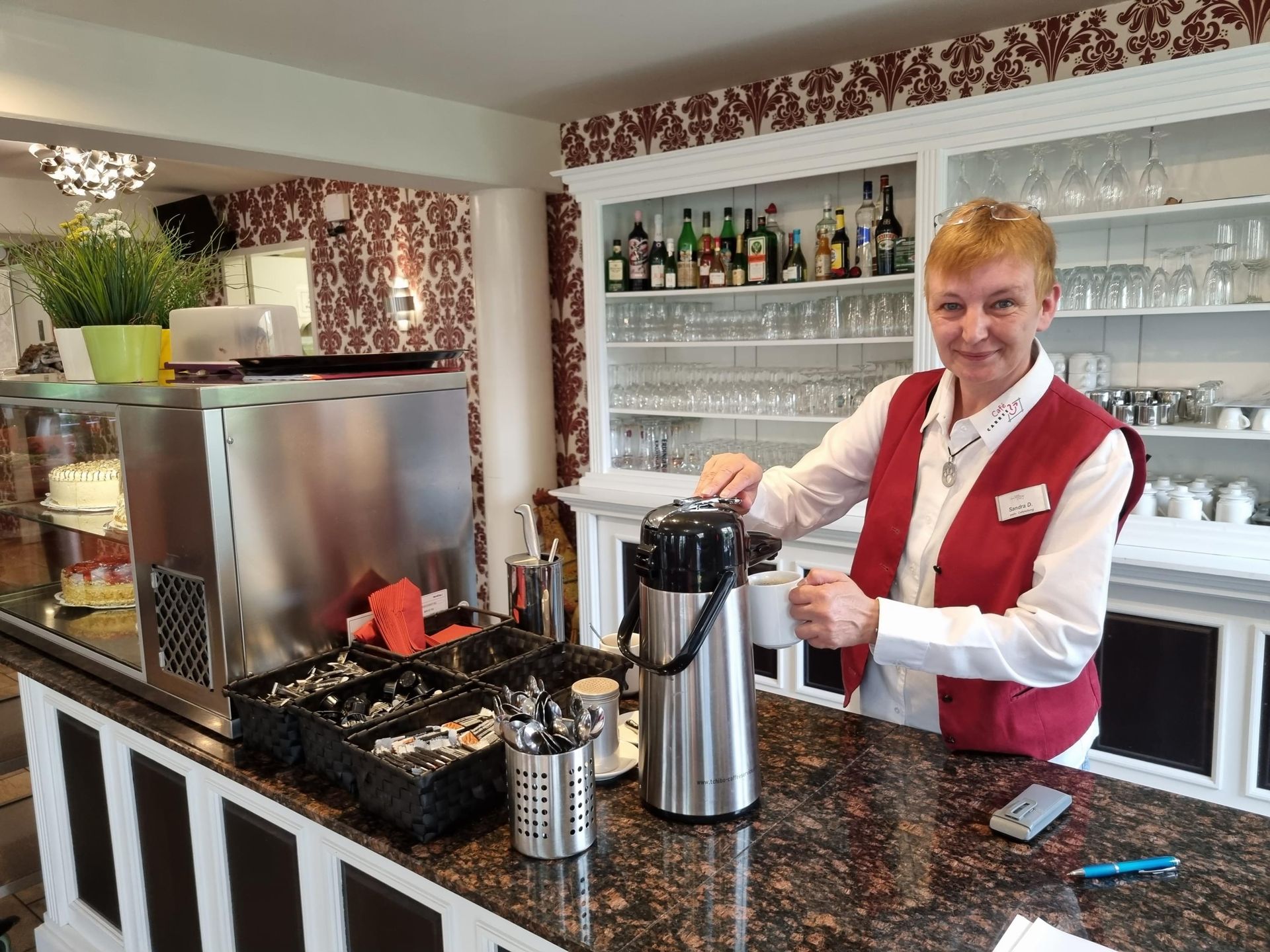 Eine Mitarbeitende blickt in Kamera, sie steht an der Getränke-Theke