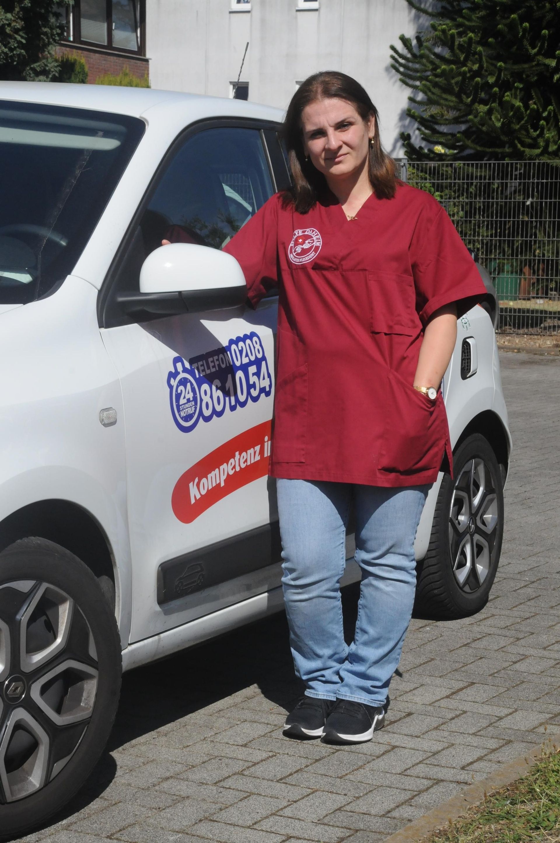 Eine Mitarbeitende blickt in Kamera, sie lehnt an einem Dienstwagen