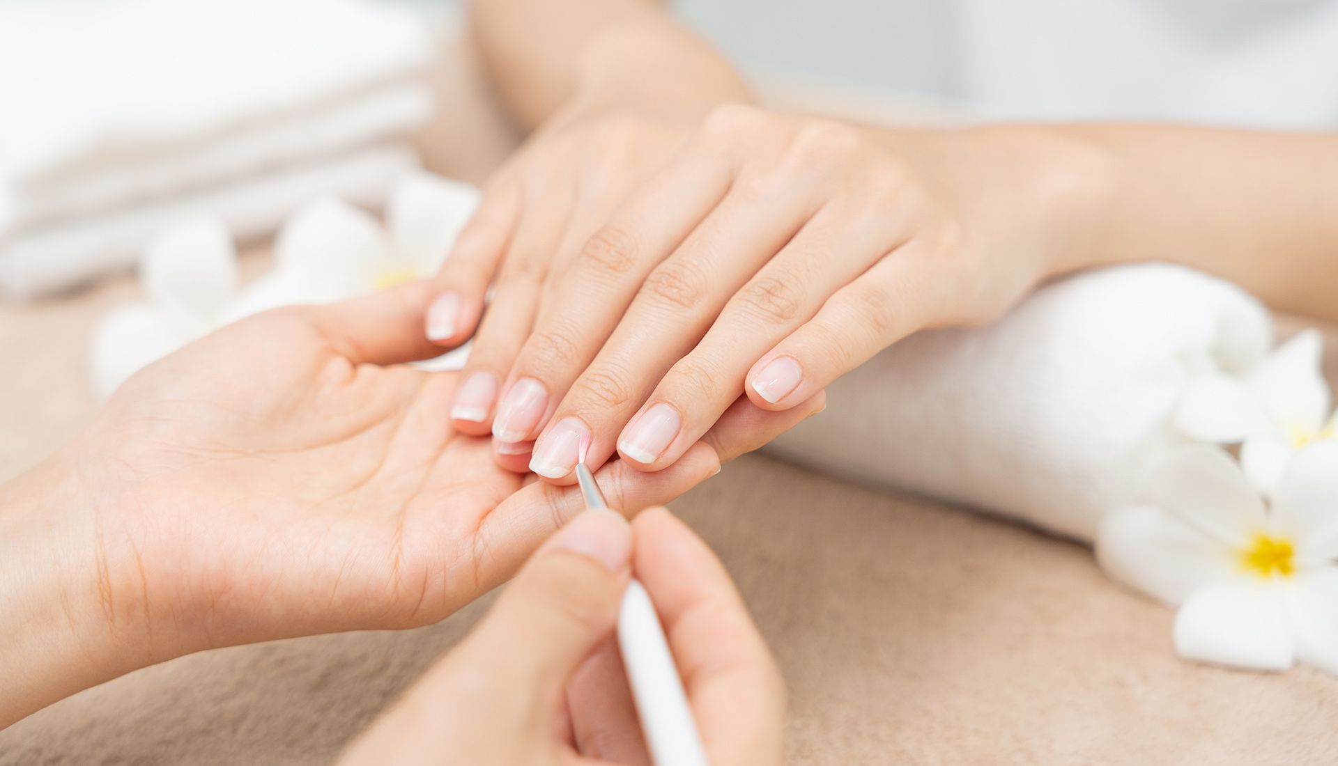 Person's hand receiving a manicure at a salon, another hand working on the nails with a tool.