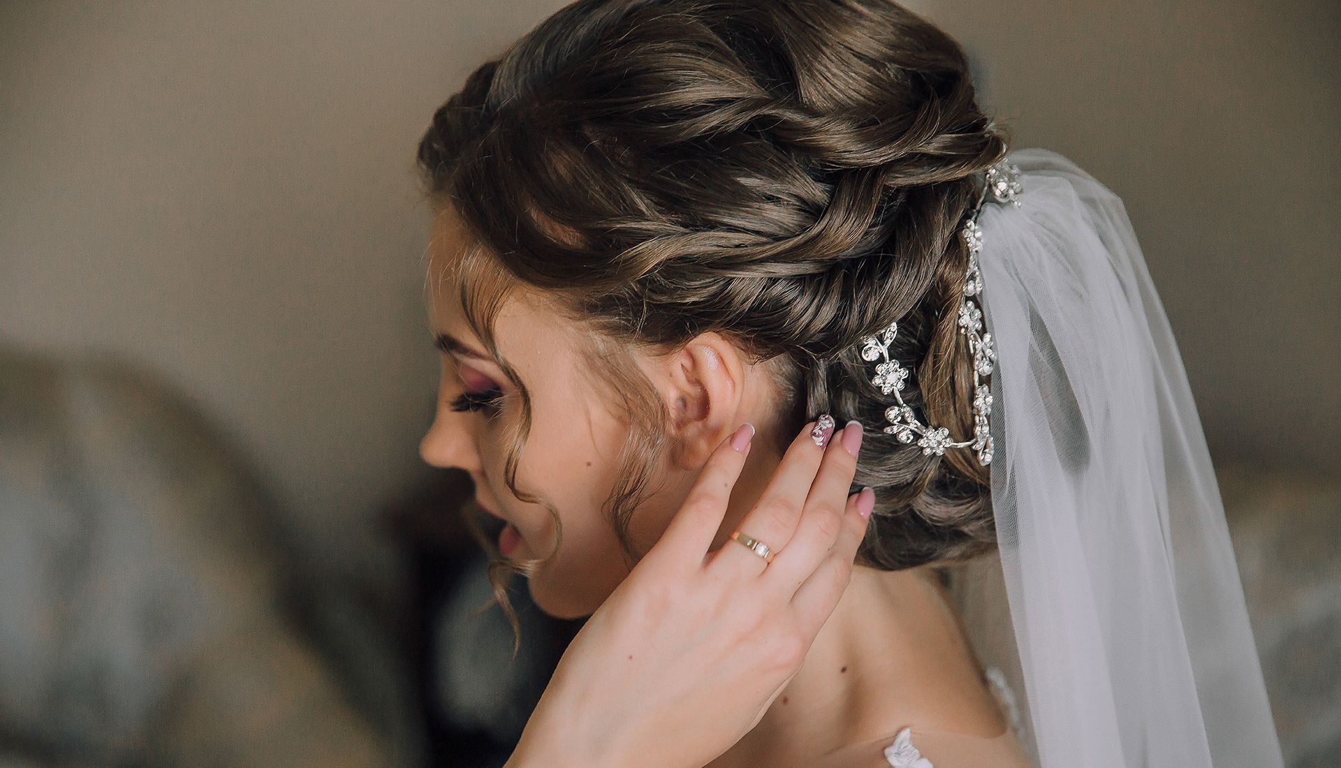 Bride with updo hairstyle, veil, and hand touching ear.