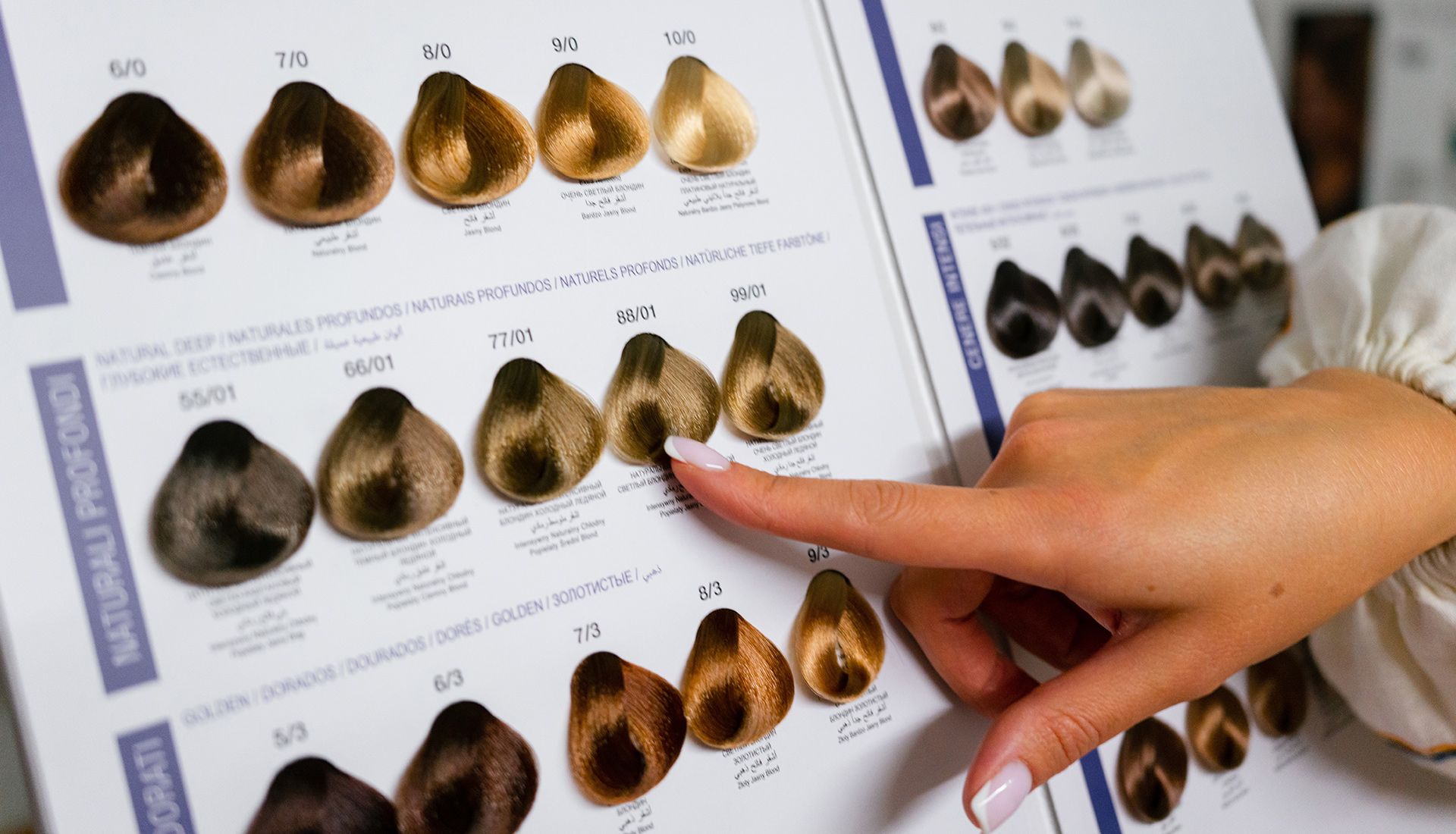 Hand pointing at a hair color swatch book, showcasing various brown and blonde dye shades.