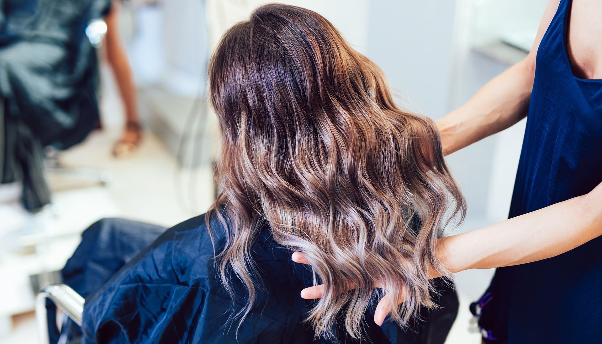 Woman in salon, hair styled with ombre effect; stylist's hands adjusting the hair.