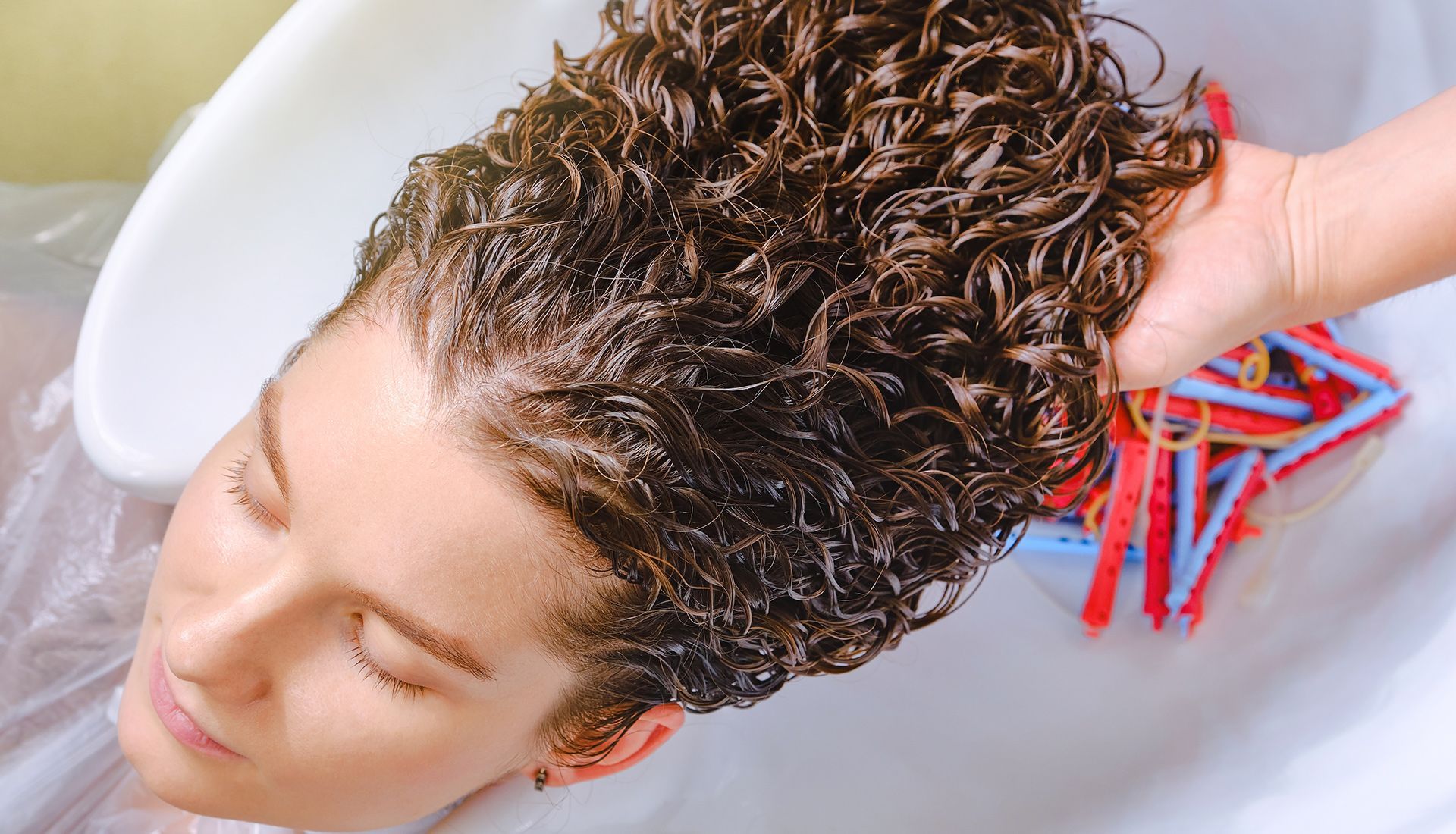 Person's head in a salon sink getting hair washed; wet, curly hair; hand holding hair.