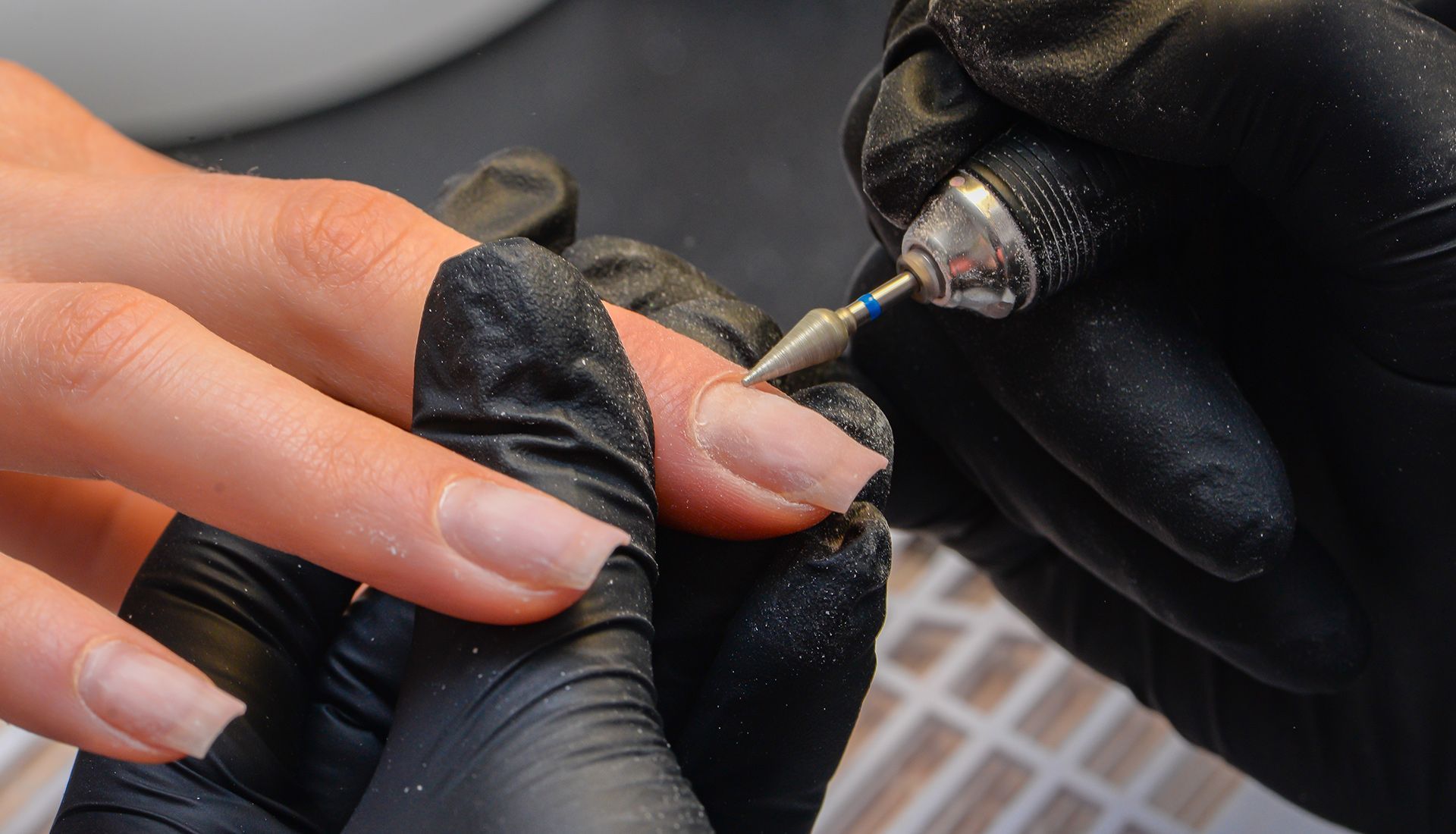 Manicurist filing a nail with a drill tool; close-up view.