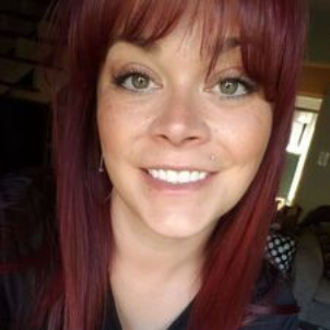 Woman with red hair and bangs smiles, freckled face, green eyes.